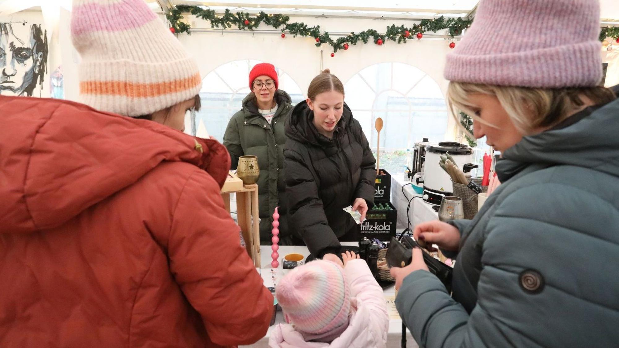 Zwei Frauen mit einem Kind an einem Stand beim Weihnachtsmarkt.