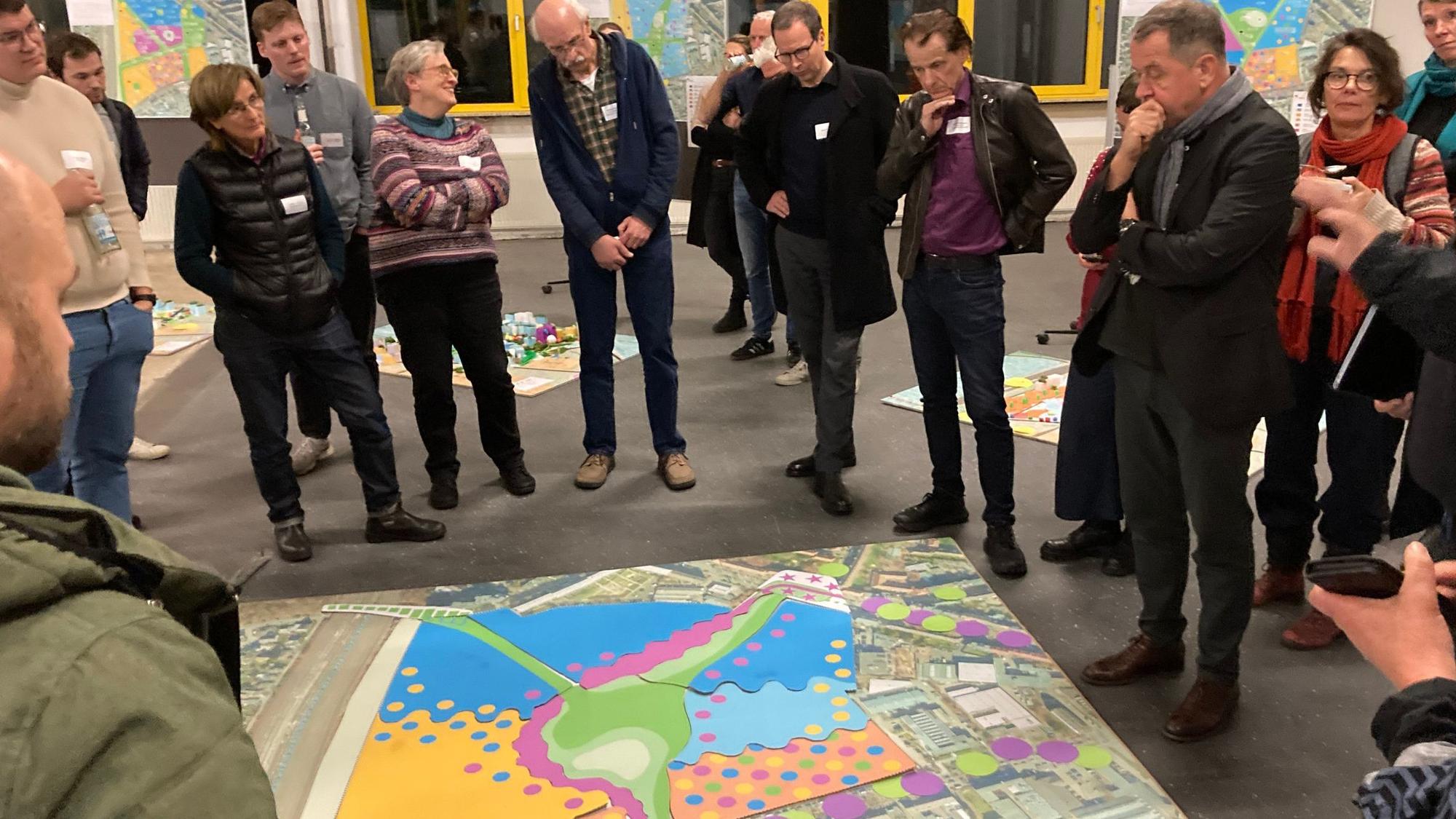 Mehrere Menschen stehen um eine große bunte Skizze, die auf dem Boden liegt, herum.