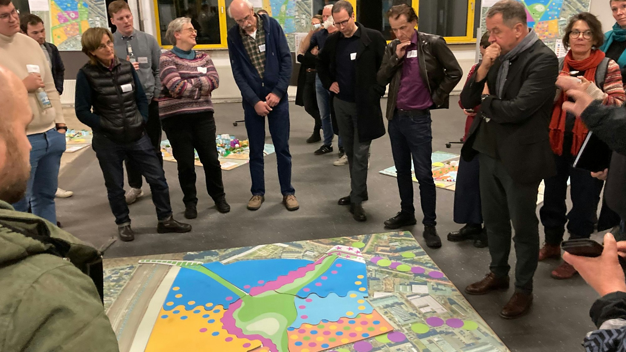 Mehrere Menschen stehen um eine große bunte Skizze, die auf dem Boden liegt, herum.