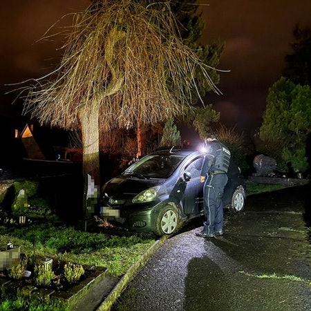 Ein Auto steht nachts auf einem Friedhof, ein Polizist daneben.