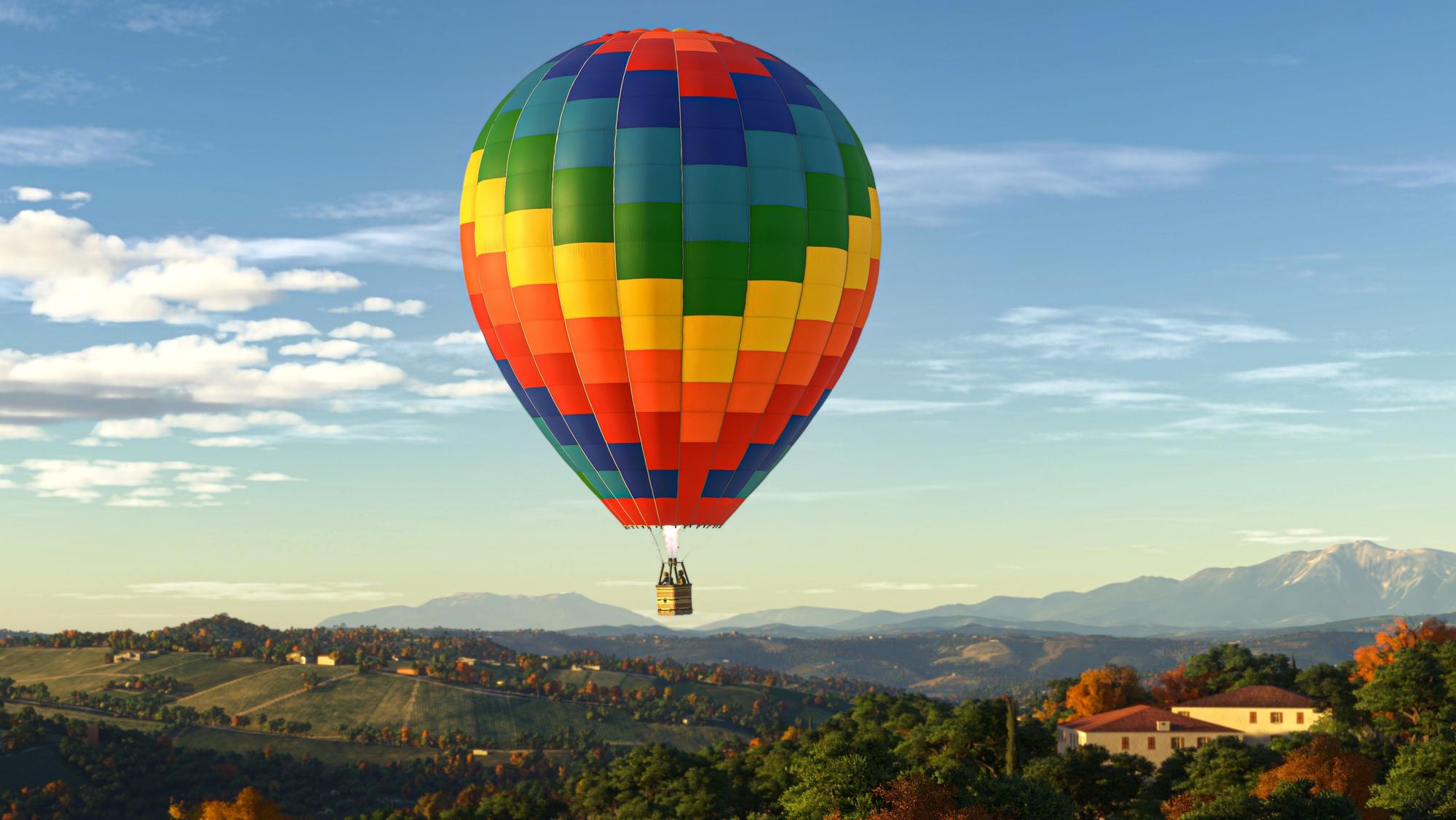 Screenshot aus dem Microsoft Flight Simulator 2024, zu sehen ist eine hügelige Landschaft, im Hintergrund Berge. Mittig schwebt ein Heißluftballon durch das Bild