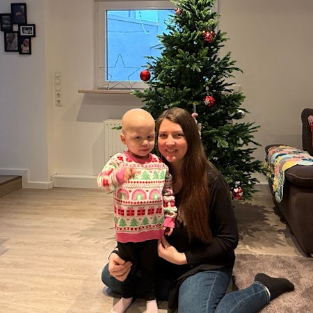 Das Foto zeigt die kleine Juna mit ihrer Mutter vor einem Weihnachtsbaum.