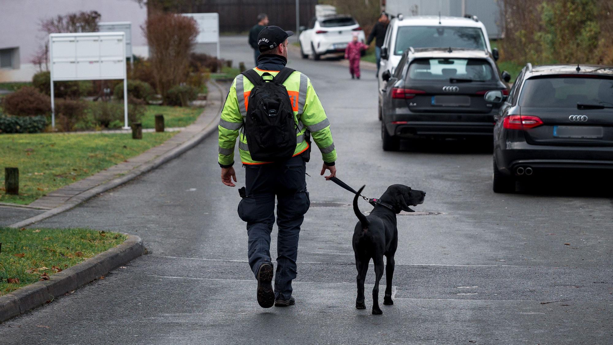 Ein Polizist geht mit einem Personenspürhund durch das Wohngebiet, in dem die tot aufgefundene Frau wohnte. (Archivbild)