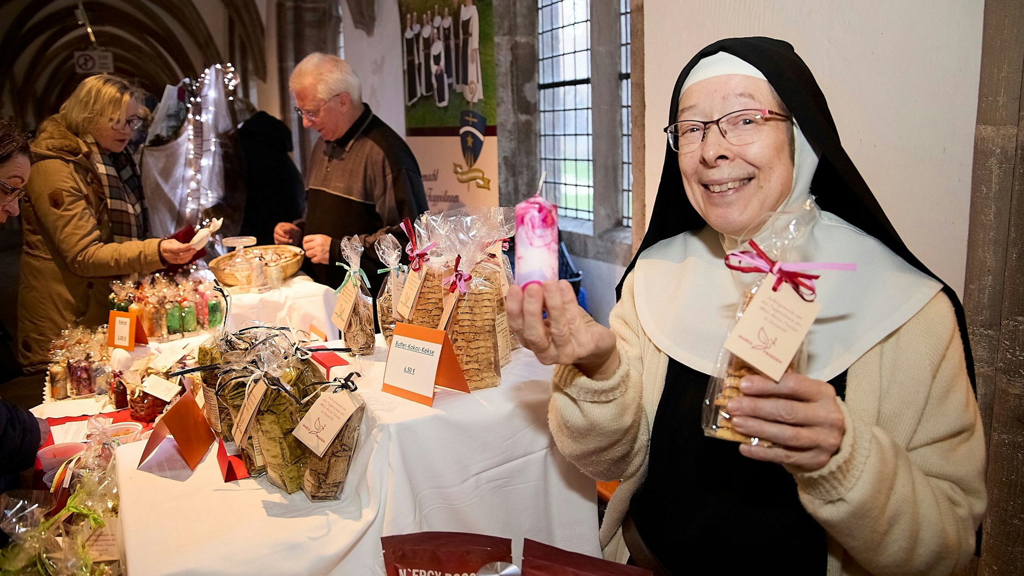 Eine Nonne hält eine Kerze und Plätzchen lächelnd in die Kamera.