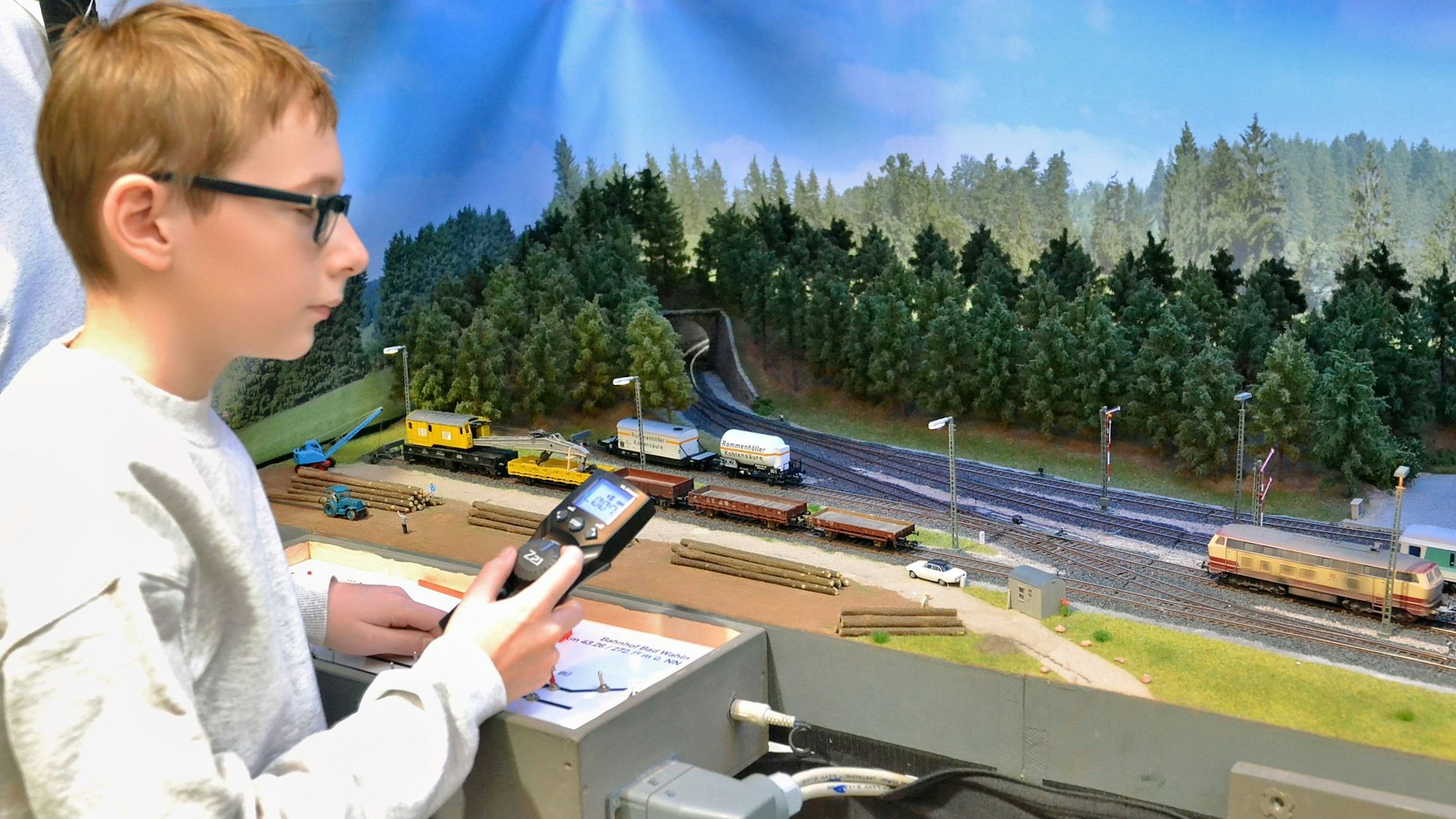 Der Junge steht mit einer Fernbedienung neben einer Modelleisenbahn.