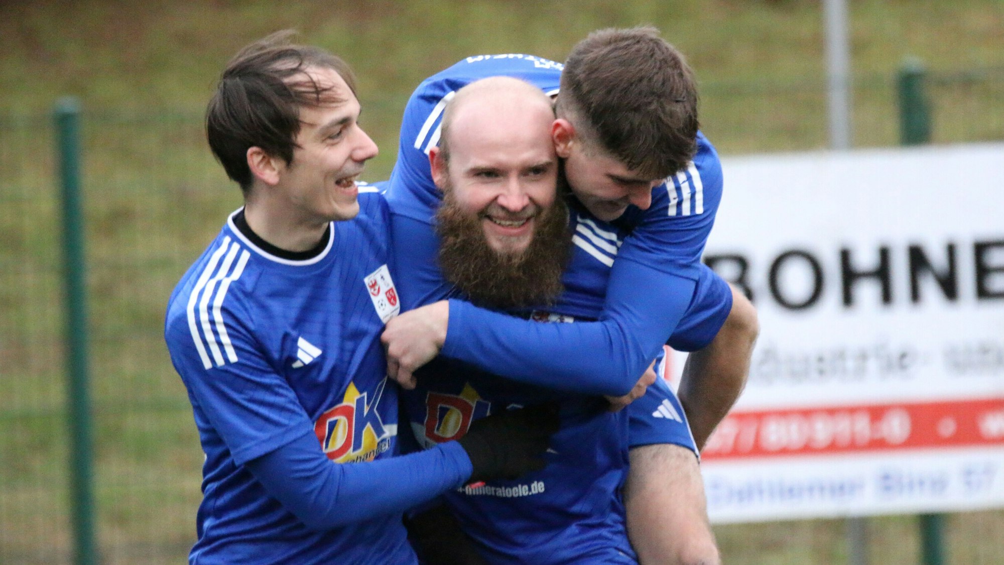 Zwei Fußballer freuen sich mit ihrem Mitspieler. Einer ist ihm auf den Rücken gesprungen.