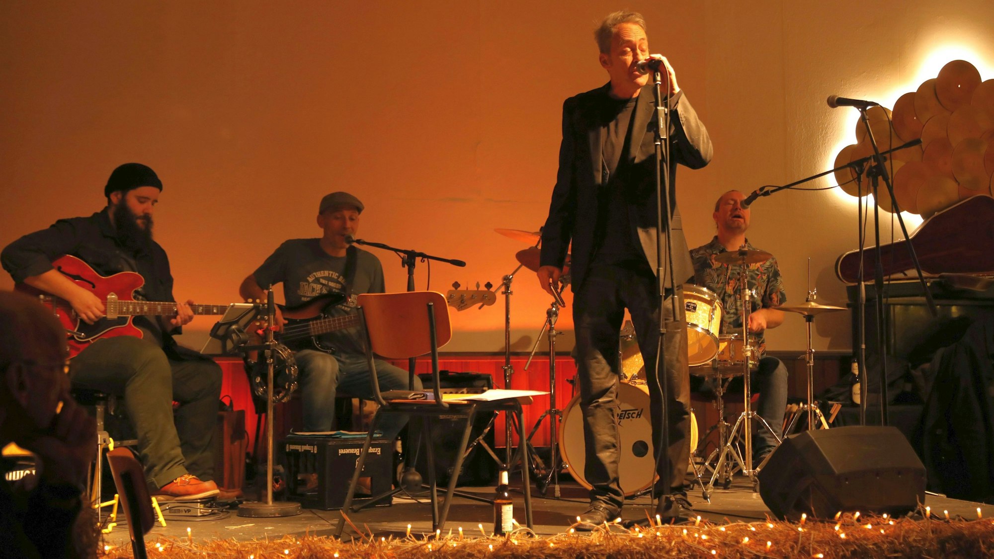 Ein Sänger am Mikrofon, dahinter drei sitzende Musiker.