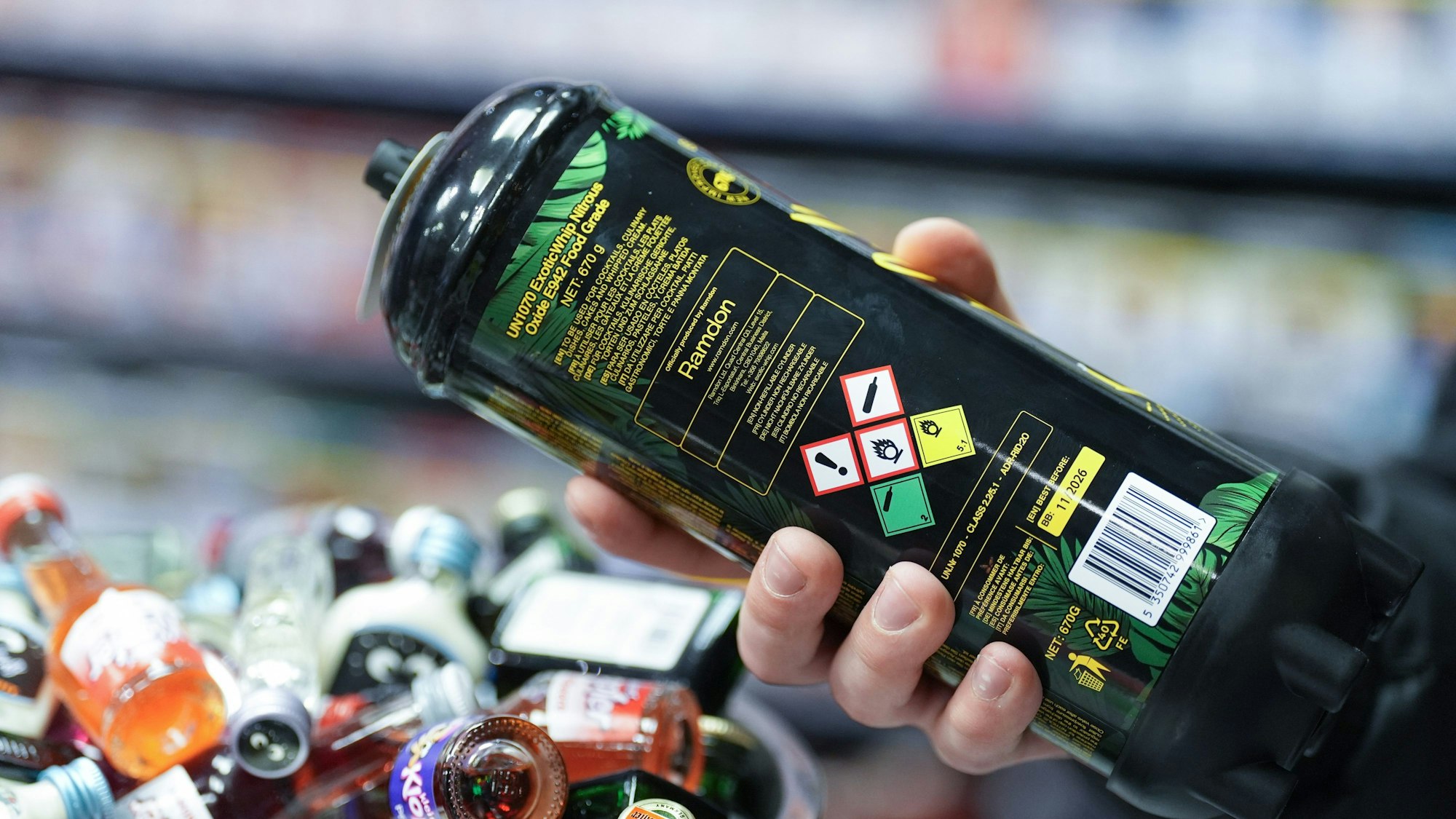 Ein Mitarbeiter hält eine Dose Lachgas am Tresen eines Kiosks in der Hand.