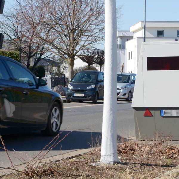 Das Bild zeigt die Messanlage, auf der Straße fährt ein Auto. Im Hintergrund stehen weitere Wagen.