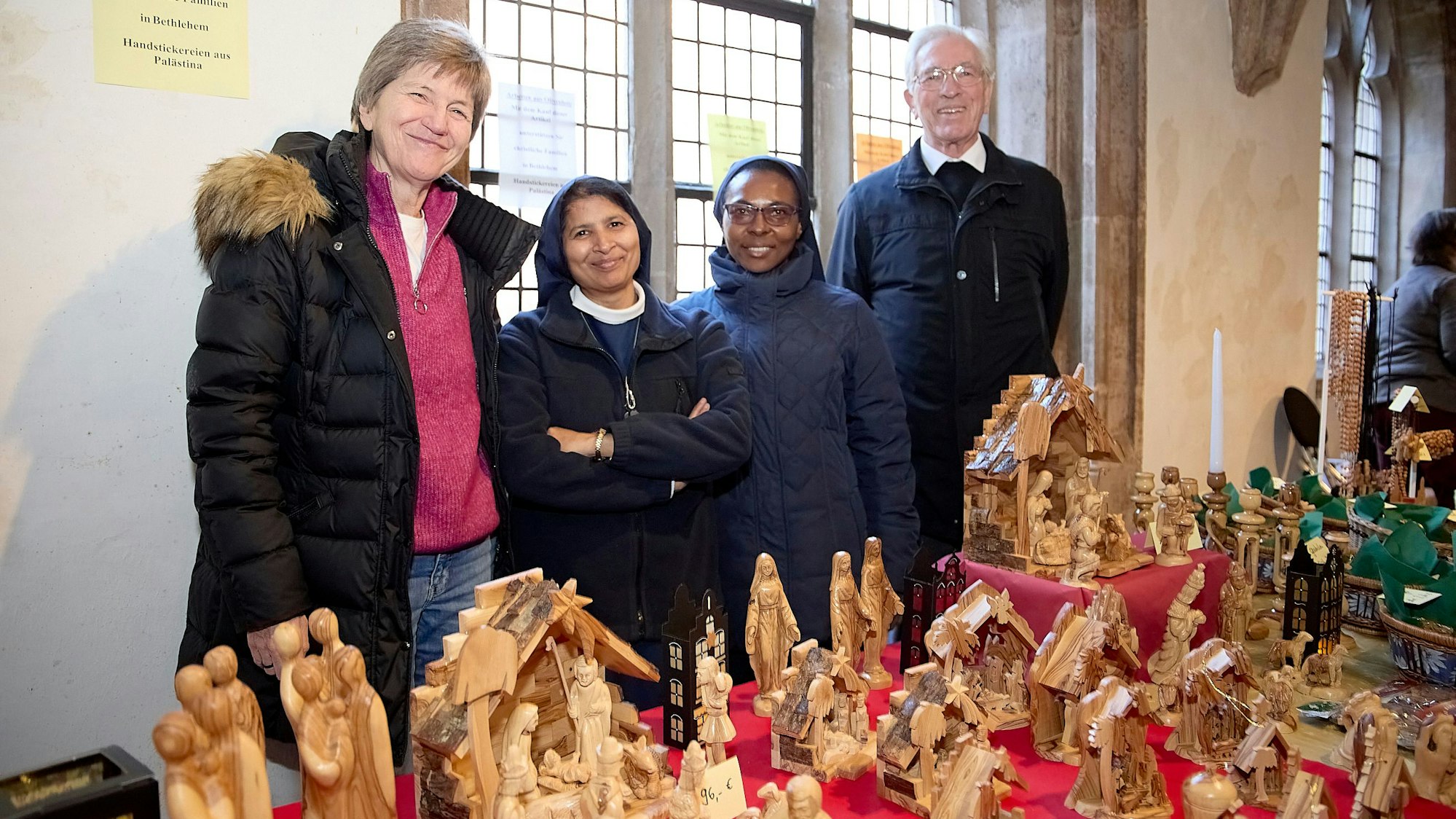 Drei Frauen und ein Mann stehen hinter Tischen, auf denen Krippenfiguren stehen.