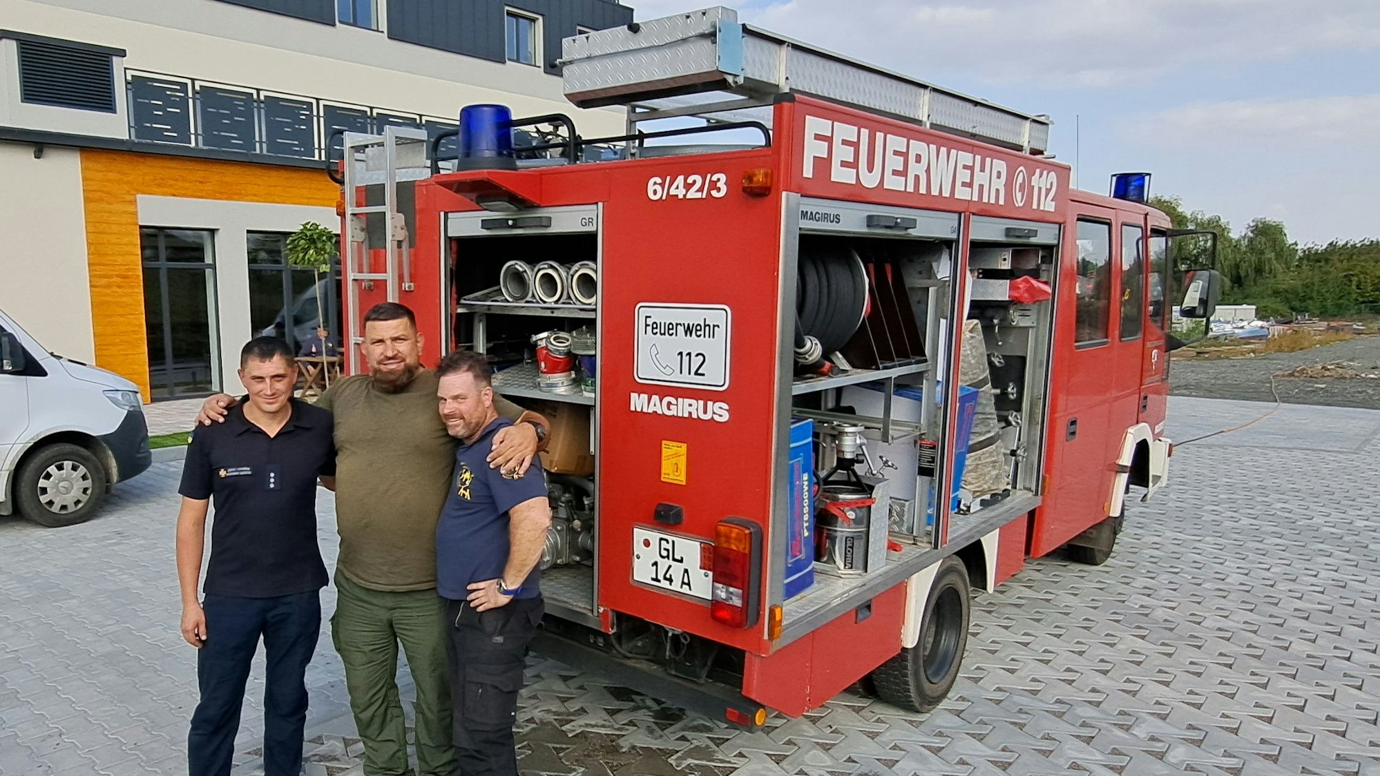 Drei Männer stehen vor einem Feuerwehrauto aus Kürten-Biesfeld am Ziel in der Ukraine.