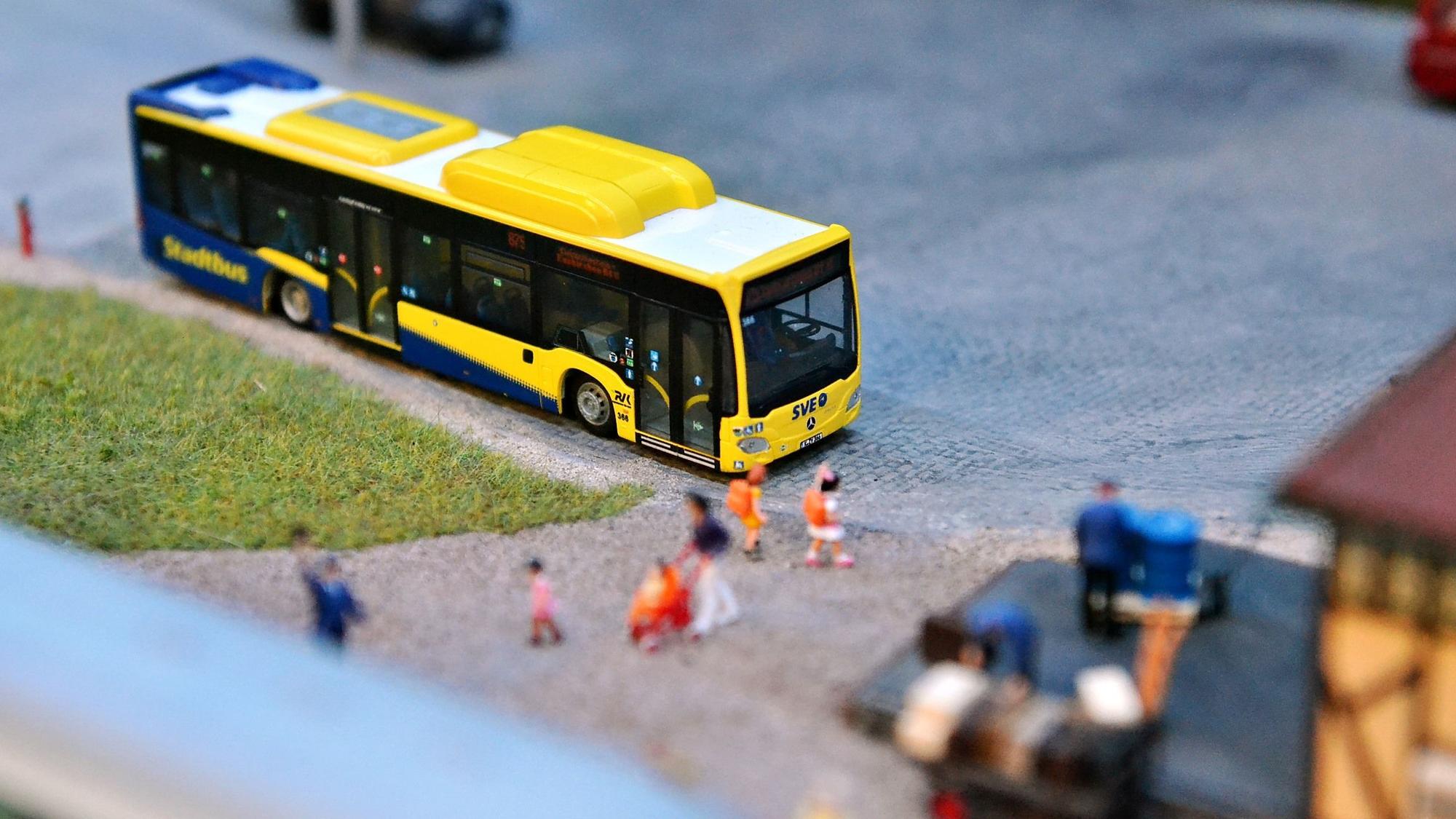 Ein gelber Miniaturbus steht in einer Modelllandschaft.