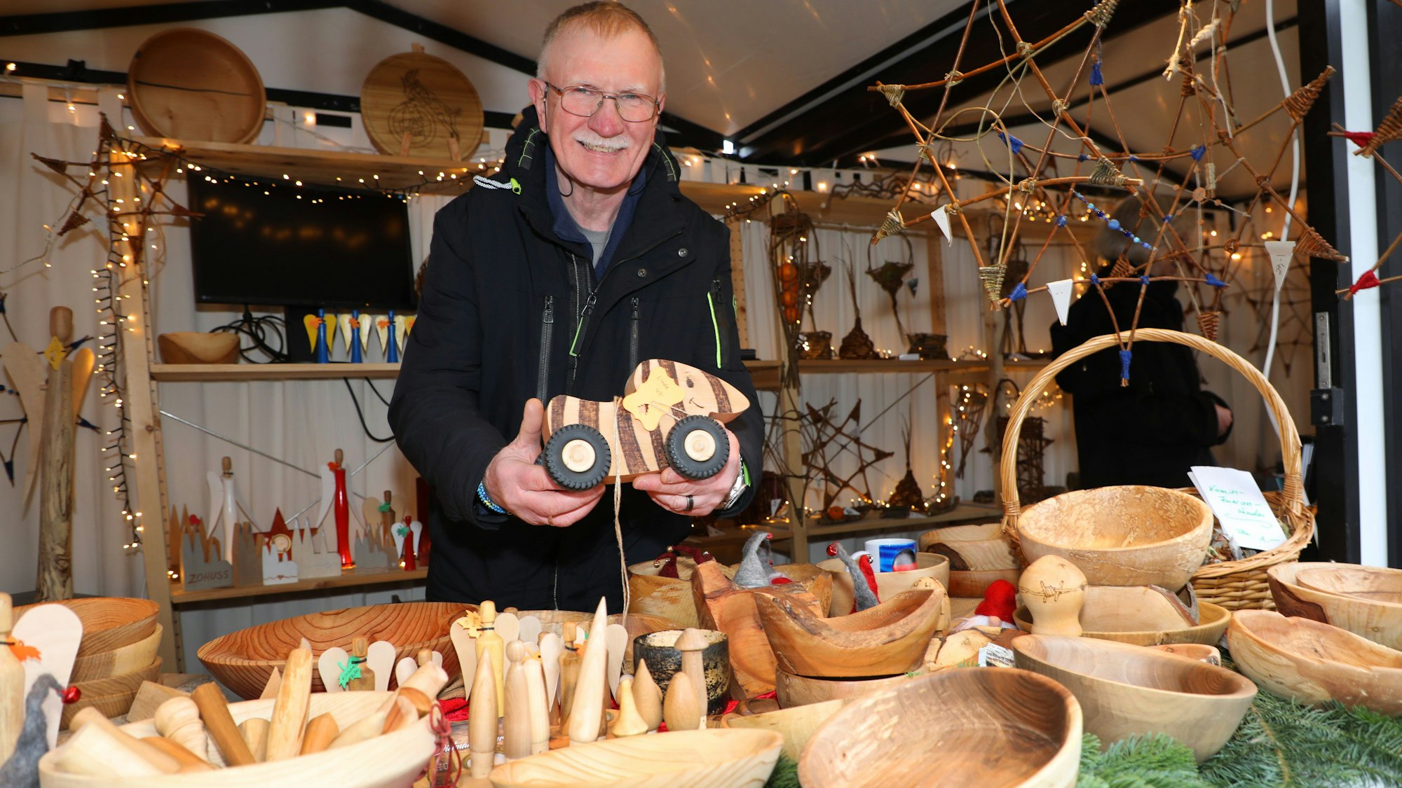 Holzkünstler Dietmar Schur hält eine Tigerente aus Holz hinter den Auslagen seines Standes auf dem Altenberger Adventsmarkt in die Höhe.