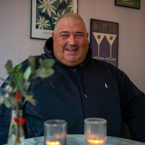 DJ Paytric (Patrick Strunk) sitzt in schwarzem Hoodie an einem Café-Tisch. Vor ihm stehen Kerzen und wiehnachtliche Blumen.