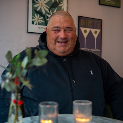 DJ Paytric (Patrick Strunk) sitzt in schwarzem Hoodie an einem Café-Tisch. Vor ihm stehen Kerzen und wiehnachtliche Blumen.