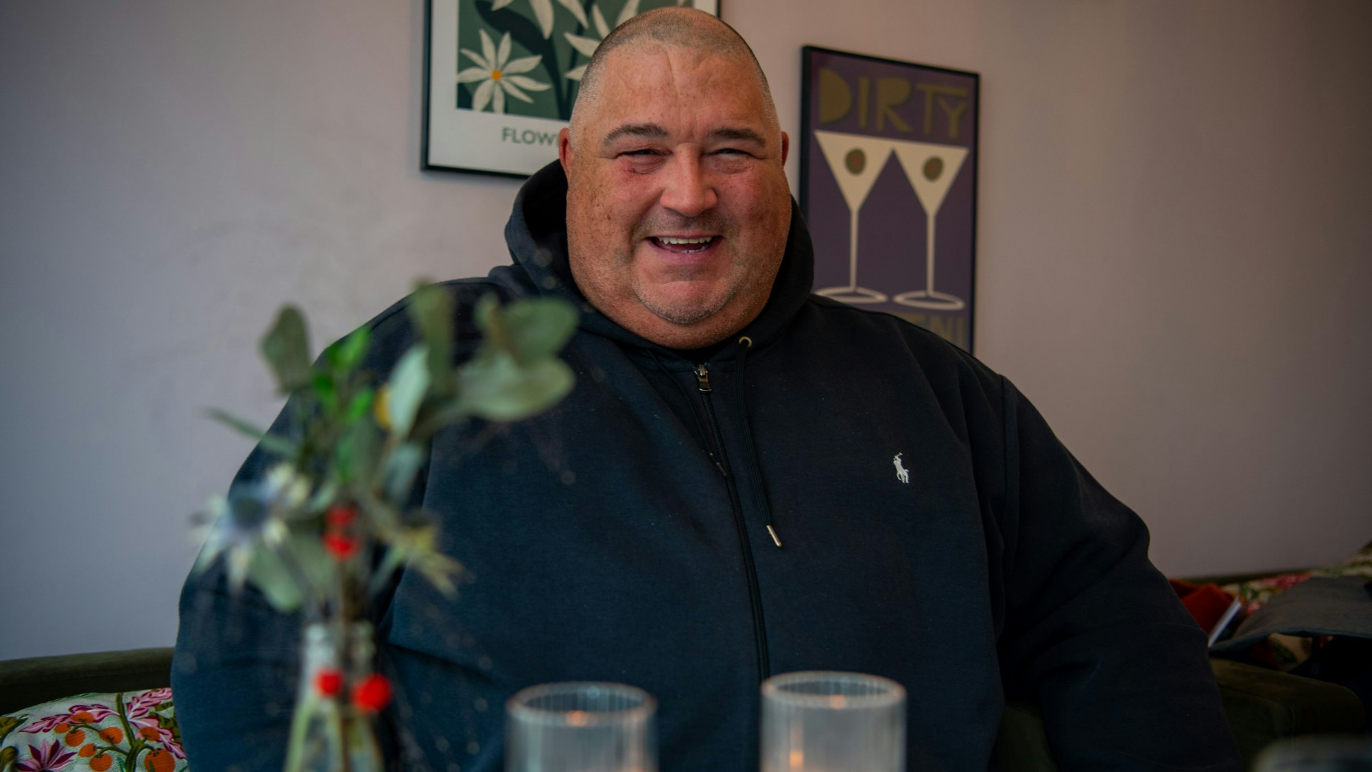 DJ Paytric (Patrick Strunk) sitzt in schwarzem Hoodie an einem Café-Tisch. Vor ihm stehen Kerzen und wiehnachtliche Blumen.