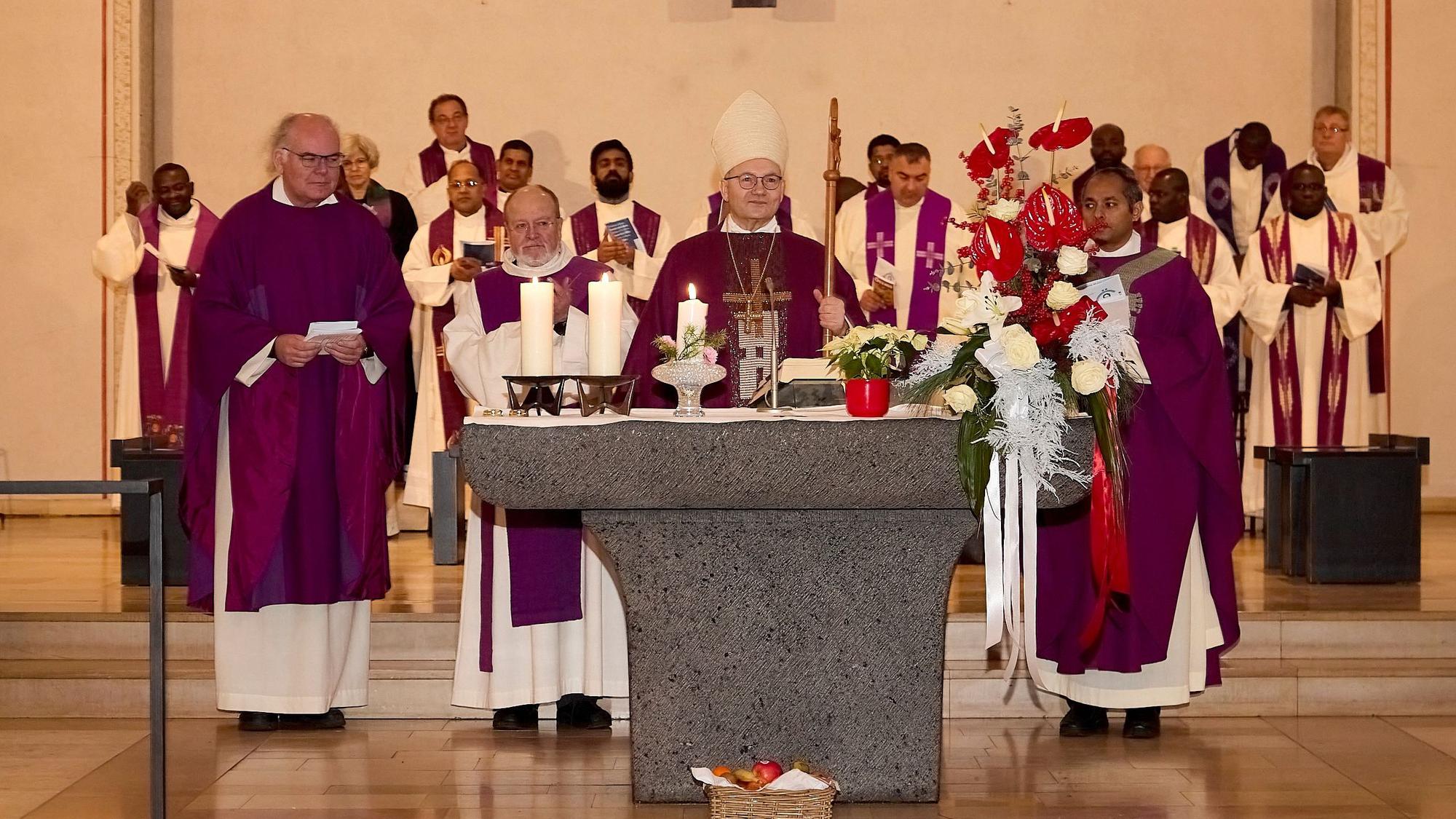 Der Aachener Bischof mit drei Konzelebranten am Altar, vor dem ein Korb mit Obst steht. Im Hintergrund zahlreiche weitere kircheliche Würdenträger.