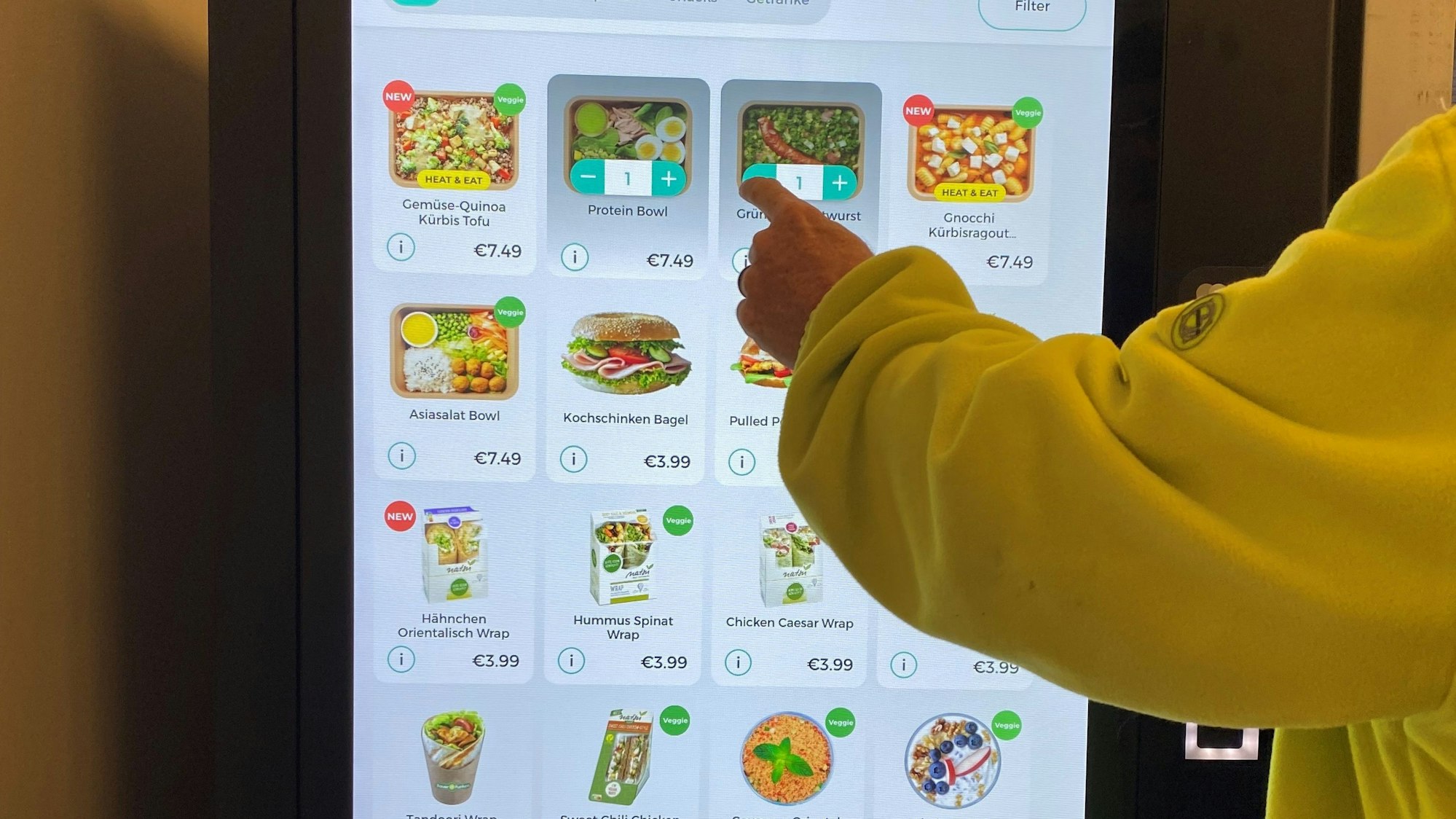 Das Foto zeigt eine Person, die den Touchscreen eines Snackautomaten bedient.