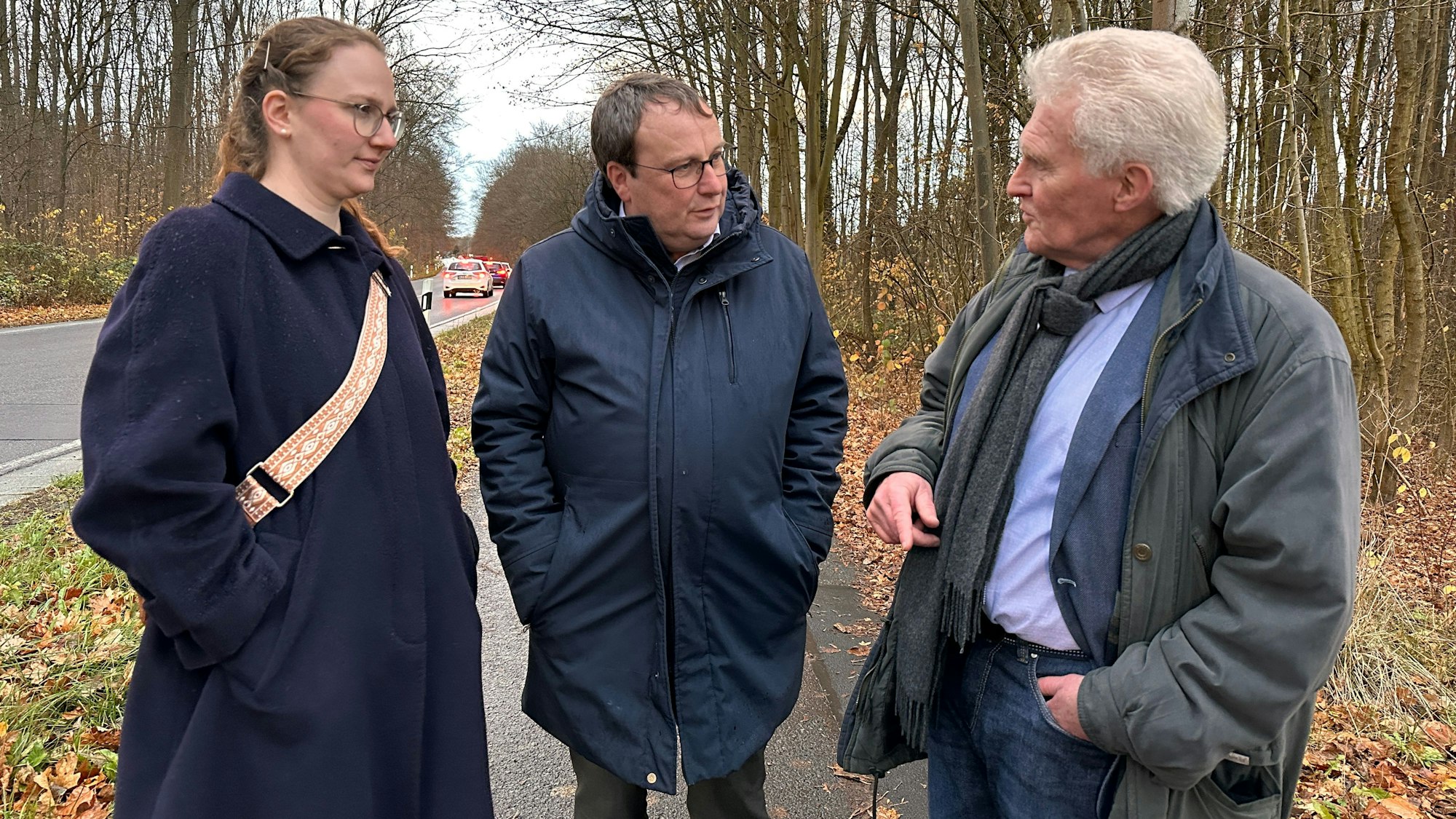 Eine Frau und zwei Männer stehen auf dem neuen Radweg an der Industriestraße in Sürth. Im Hintergrund ist ein Wald und eine befahrene Straße zu sehen.
