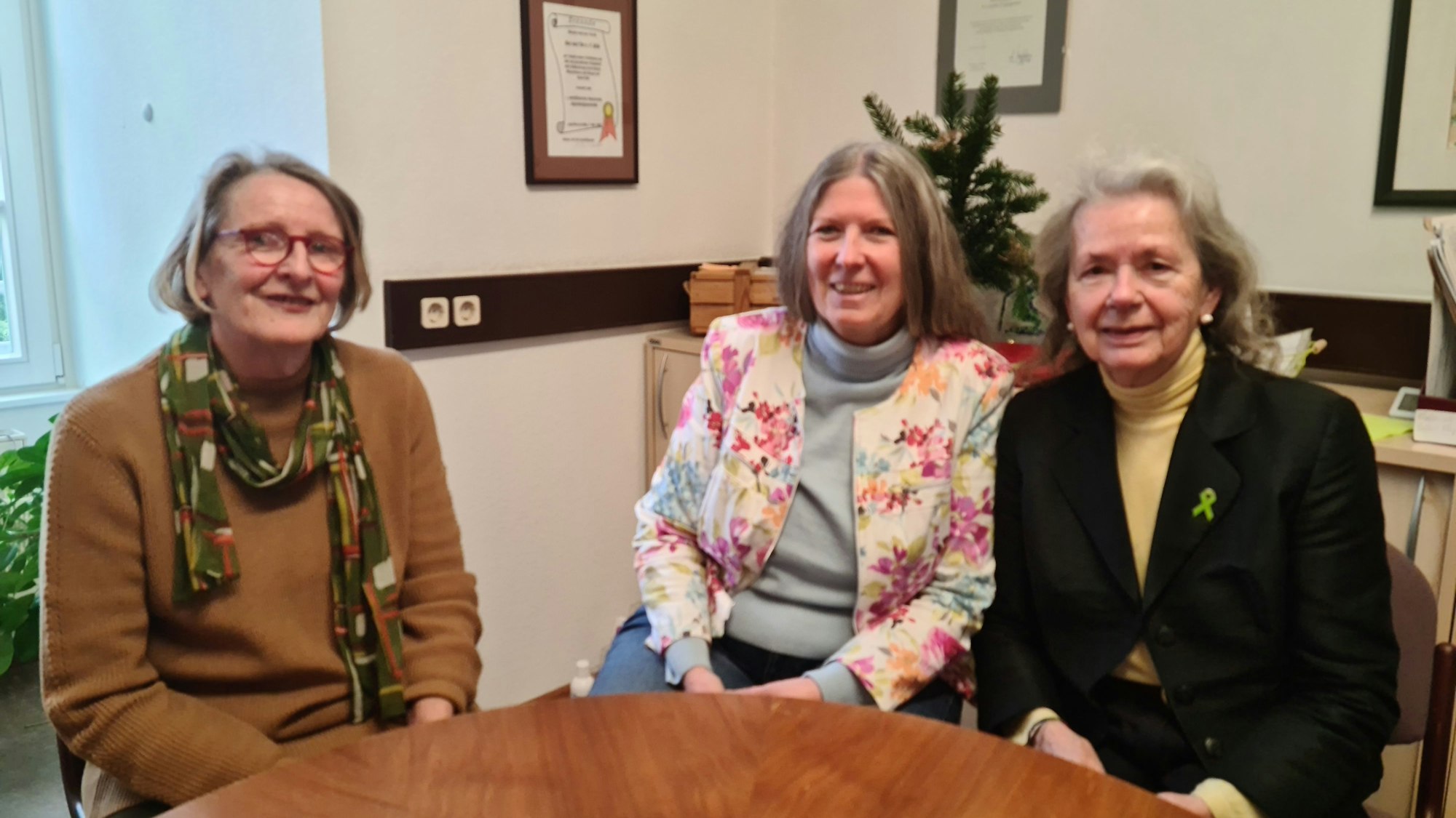 An einem runden Tisch sitzen drei Damen.