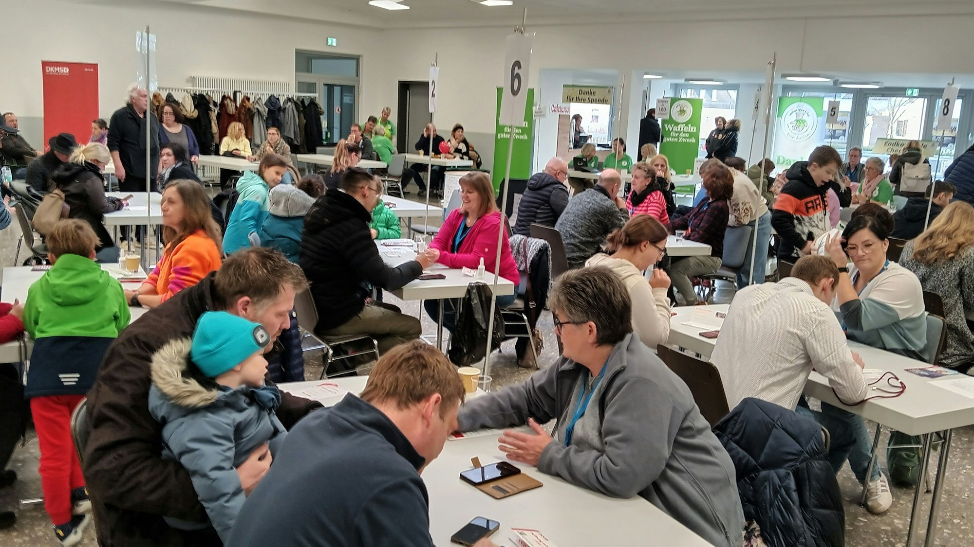 Menschen aller Altersklassen sitzen an Tischen und lassen sich das Prozedere erklären.