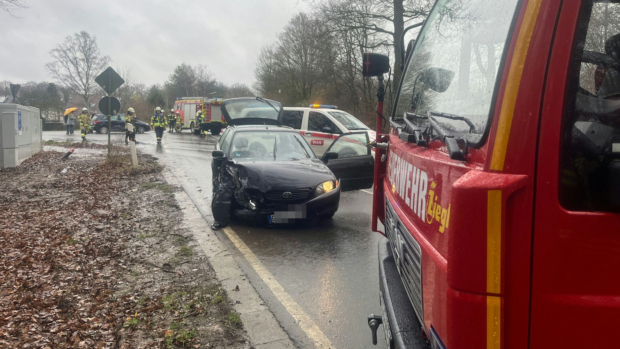 Hinter einem Feuerwehrfahrzeug steht ein schwer beschädigter Wagen.