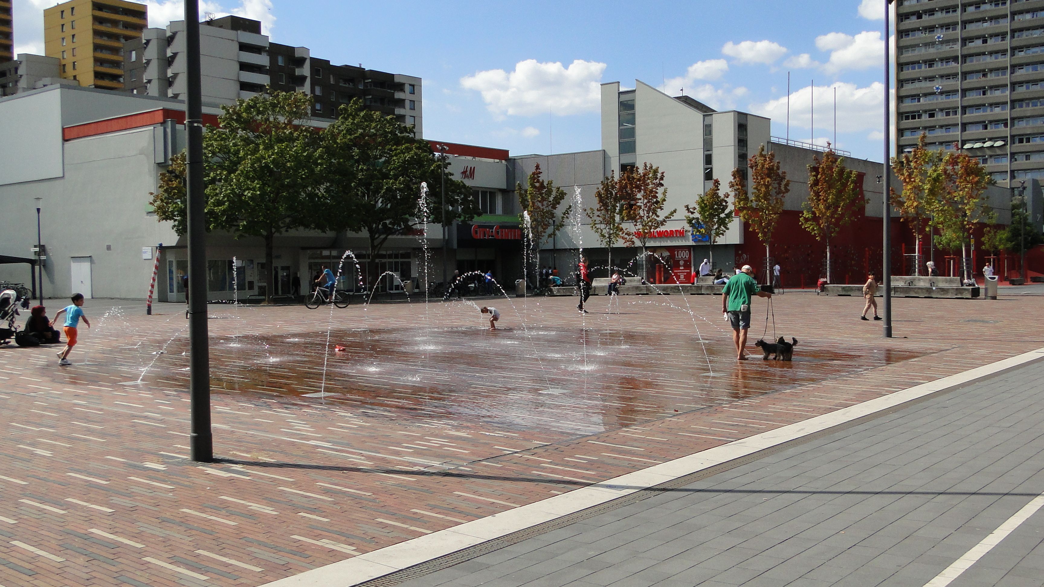 Auf einem Platz sind Wasserfontänen, Kinder spielen im Wasser.