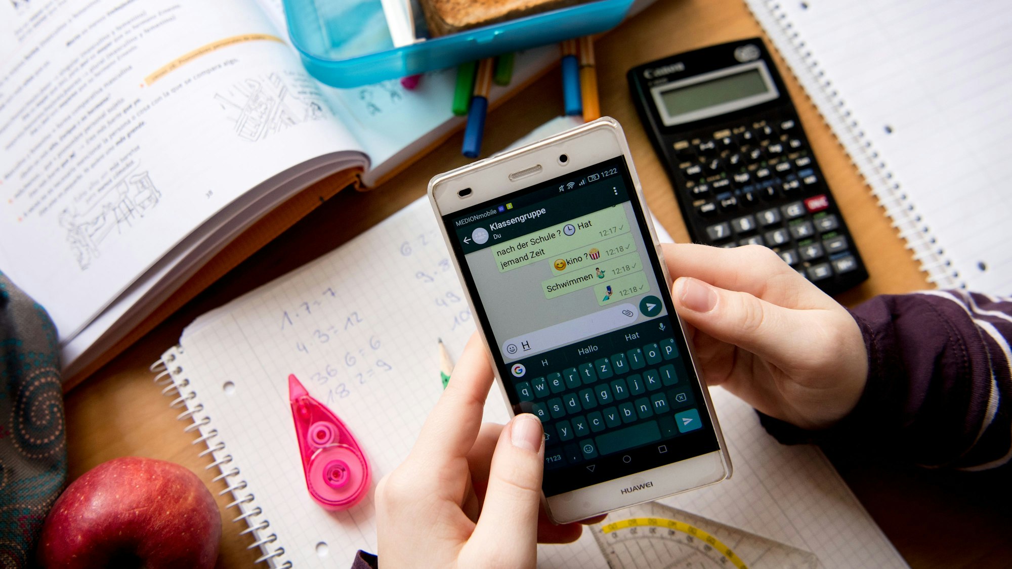 Eine Schülerin sitzt mit ihrem Handy und ihren Schulsachen an einem Schreibtisch.