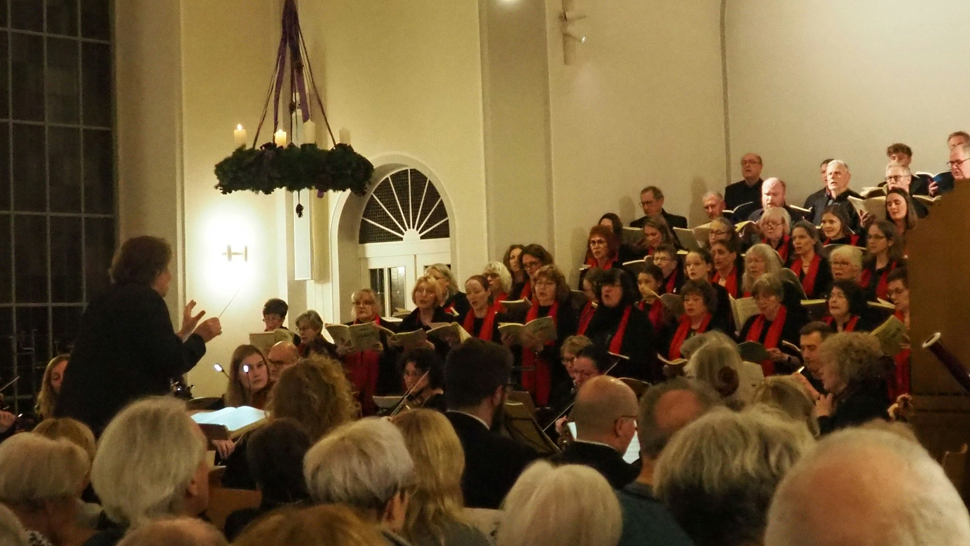 Ein Chor steht in einer Kirche unter einem Adventkranz und singt.