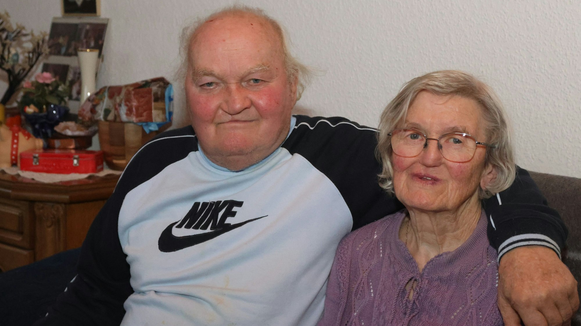 Ein älteres Ehepaar sitzt nebeneinander. Er legt seinen Arm um sie.