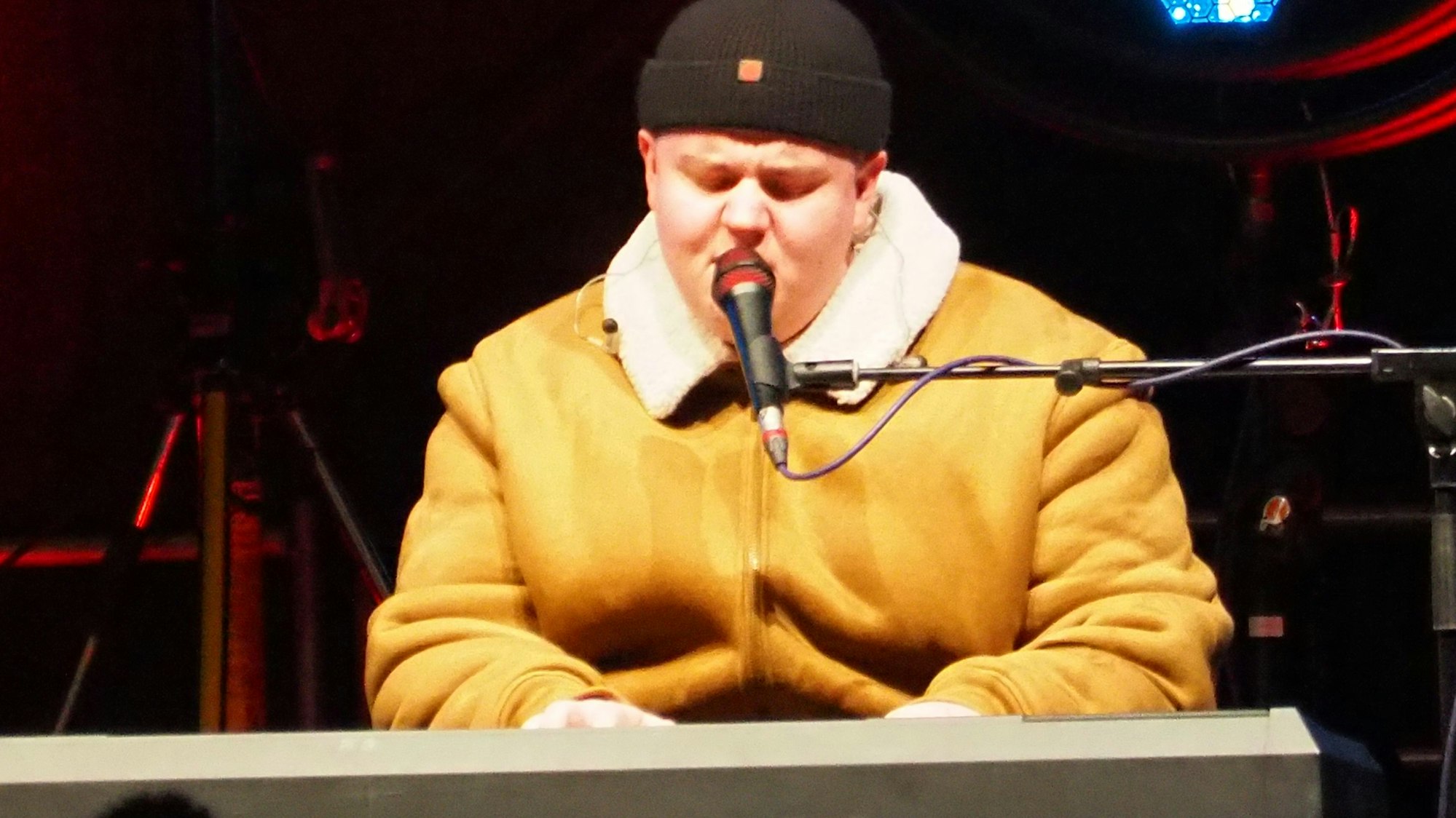 Marc Atlas sitzt am Keyboard und singt. Er trägt eine dicke Jacke und eine Mütze.