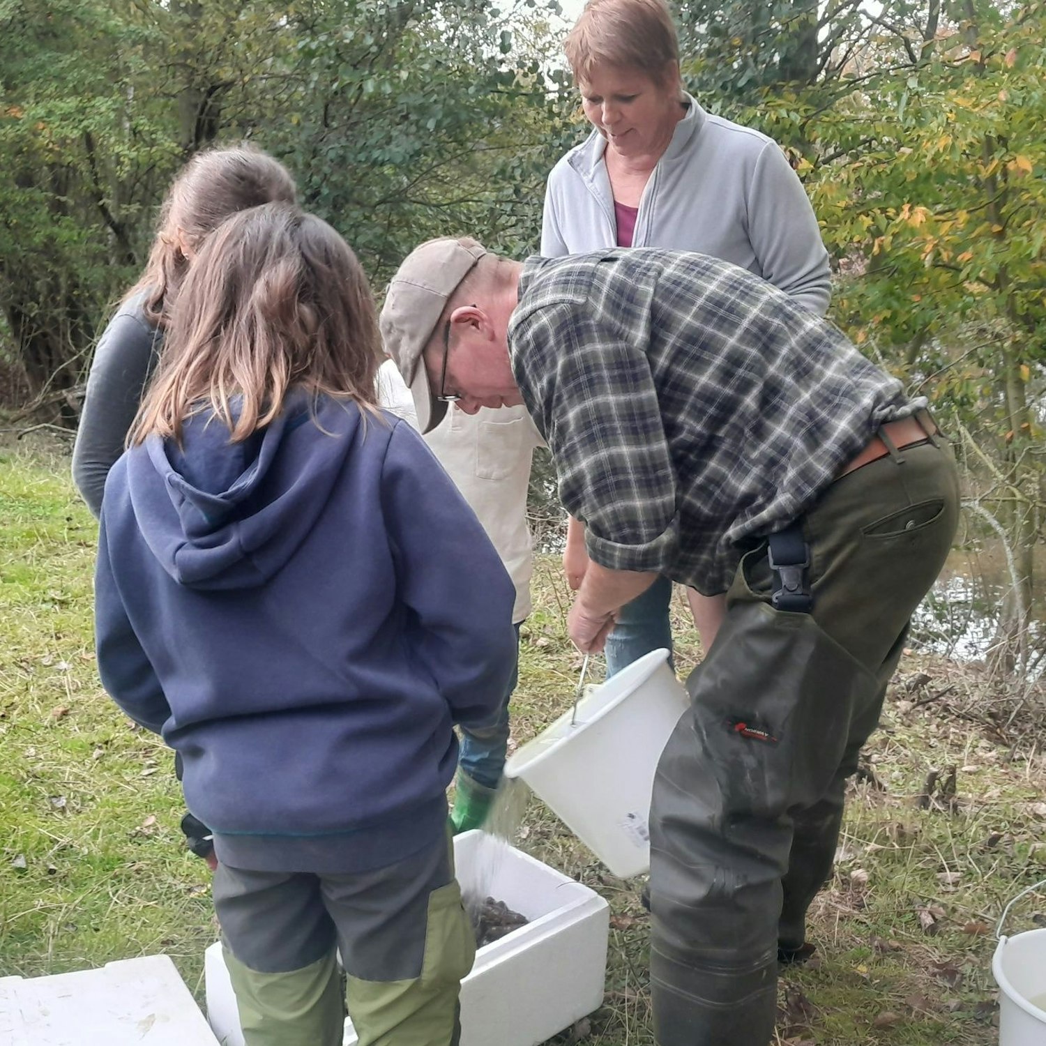 Ein Mann schüttet aus einem Eimer Wasser in einen Behälter, in dem sich Krebse befinden. Kinder und eine Frau schauen ihm dabei zu.