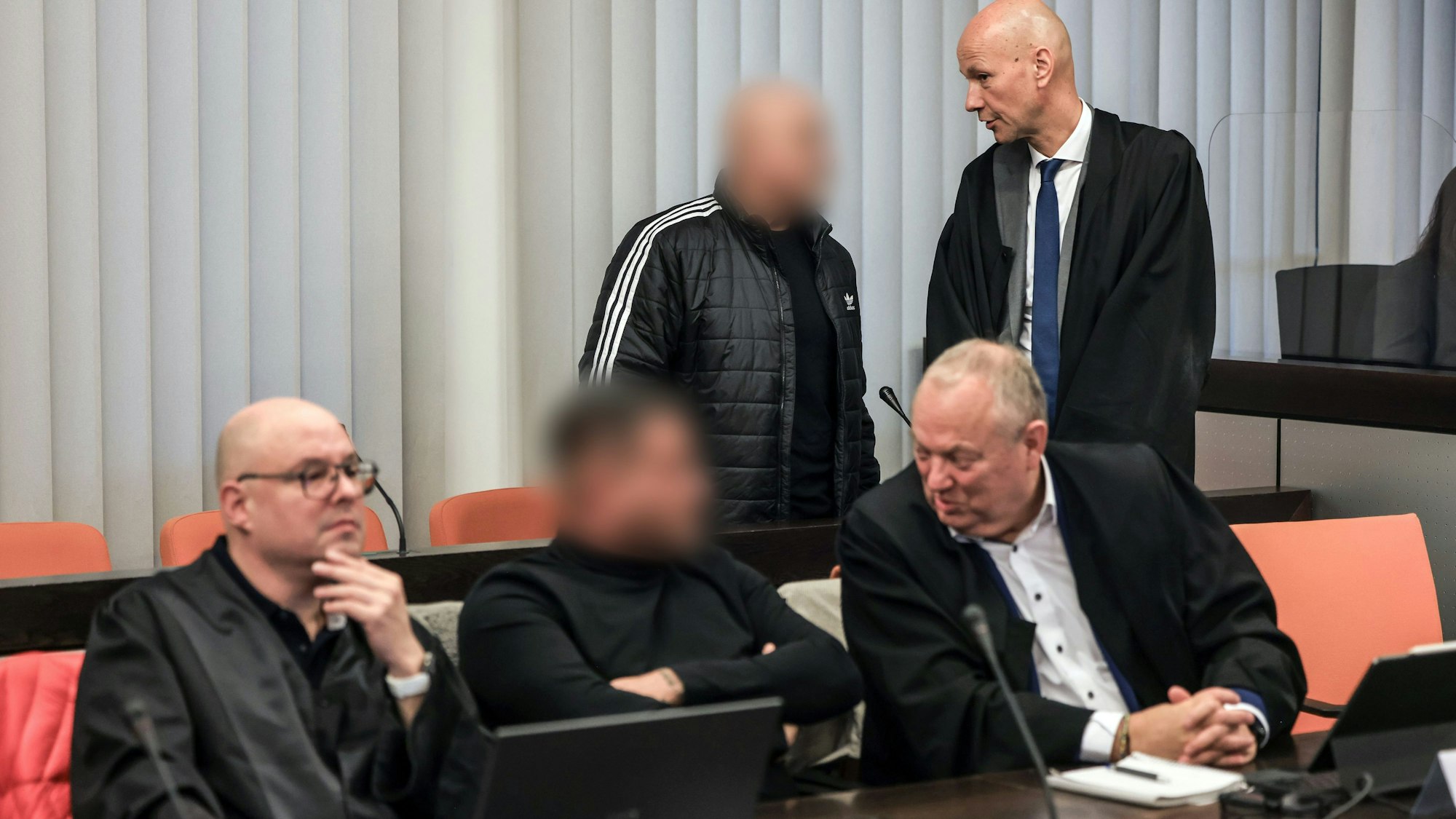 dpatopbilder - 10.12.2024, Nordrhein-Westfalen, Wuppertal: Der Hauptangeklagte (hinten, links) spricht im Gerichtssaal mit seinem Verteidiger Oliver Doelfs (hinten, rechts), während vorne ein Angeklagter (M) mit seinem Verteidiger Hartmut Moyzio (vorne, rechts) spricht. In Wuppertal hat der Prozess wegen eines Erpressungsversuchs gegen die Familie von Ex-Formel-1-Weltmeister Michael Schumacher begonnen. Angeklagt sind drei 30 bis 53 Jahre alte Männer. Dem Haupttäter wird versuchte Erpressung in einem besonders schweren Fall vorgeworfen, den beiden anderen Beihilfe dazu. Foto: Oliver Berg/dpa - ACHTUNG: Person(en) wurde(n) aus rechtlichen Gründen gepixelt +++ dpa-Bildfunk +++