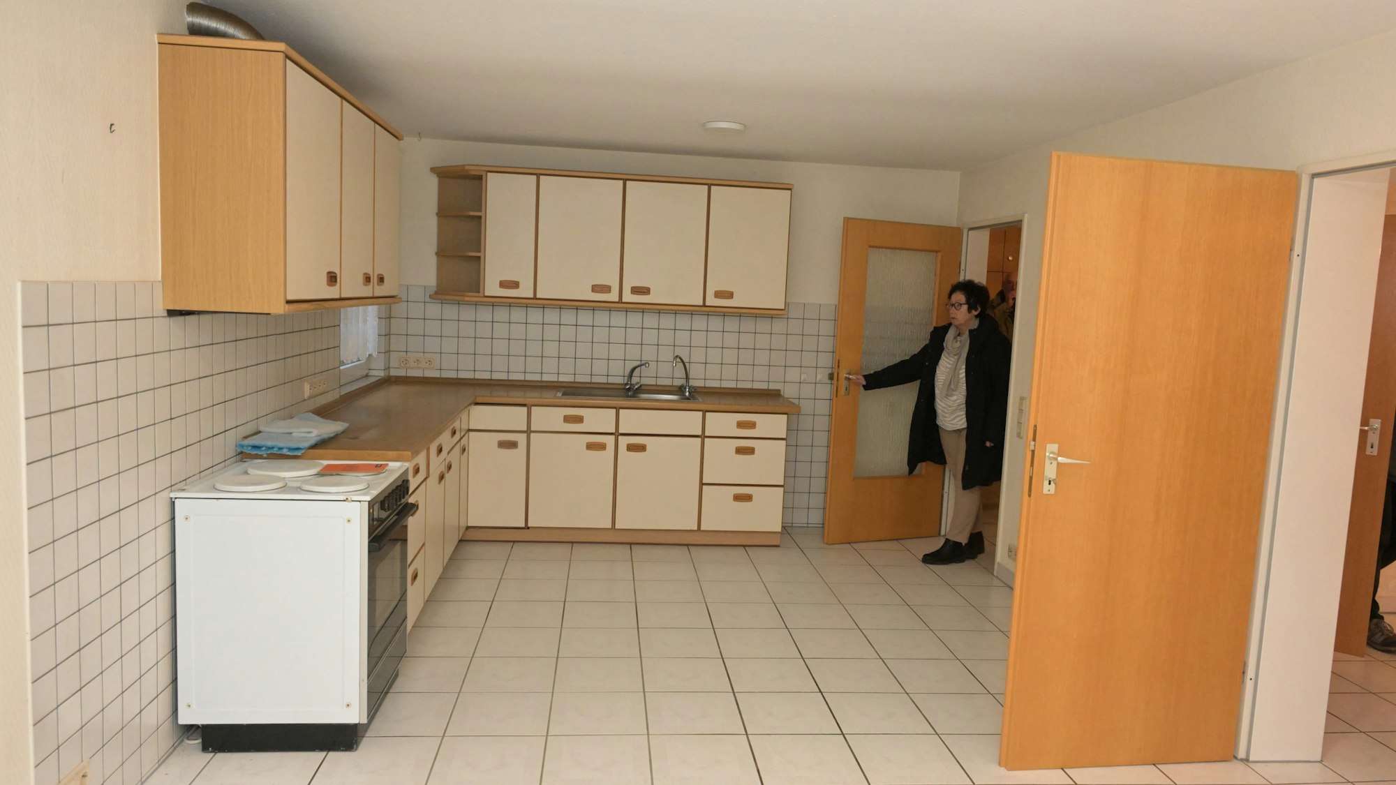 Eine Frau betritt eine Küche mit einer Küchenzeile aus hellem Holz.