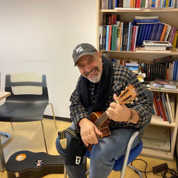 Der Musiker Vassil Svechtarov sitzt mit einem Saiteninstrument in den Händen vor einem Regal mit Büchern.