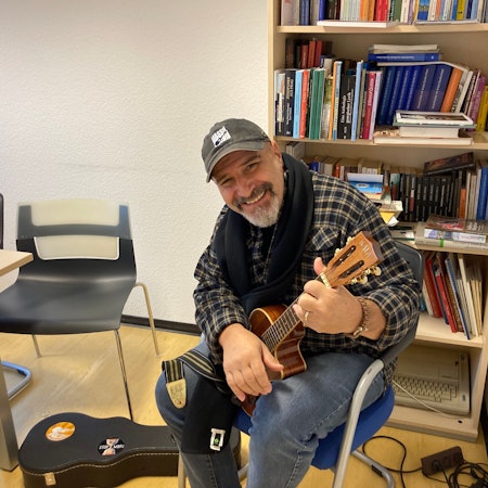 Der Musiker Vassil Svechtarov sitzt mit einem Saiteninstrument in den Händen vor einem Regal mit Büchern.