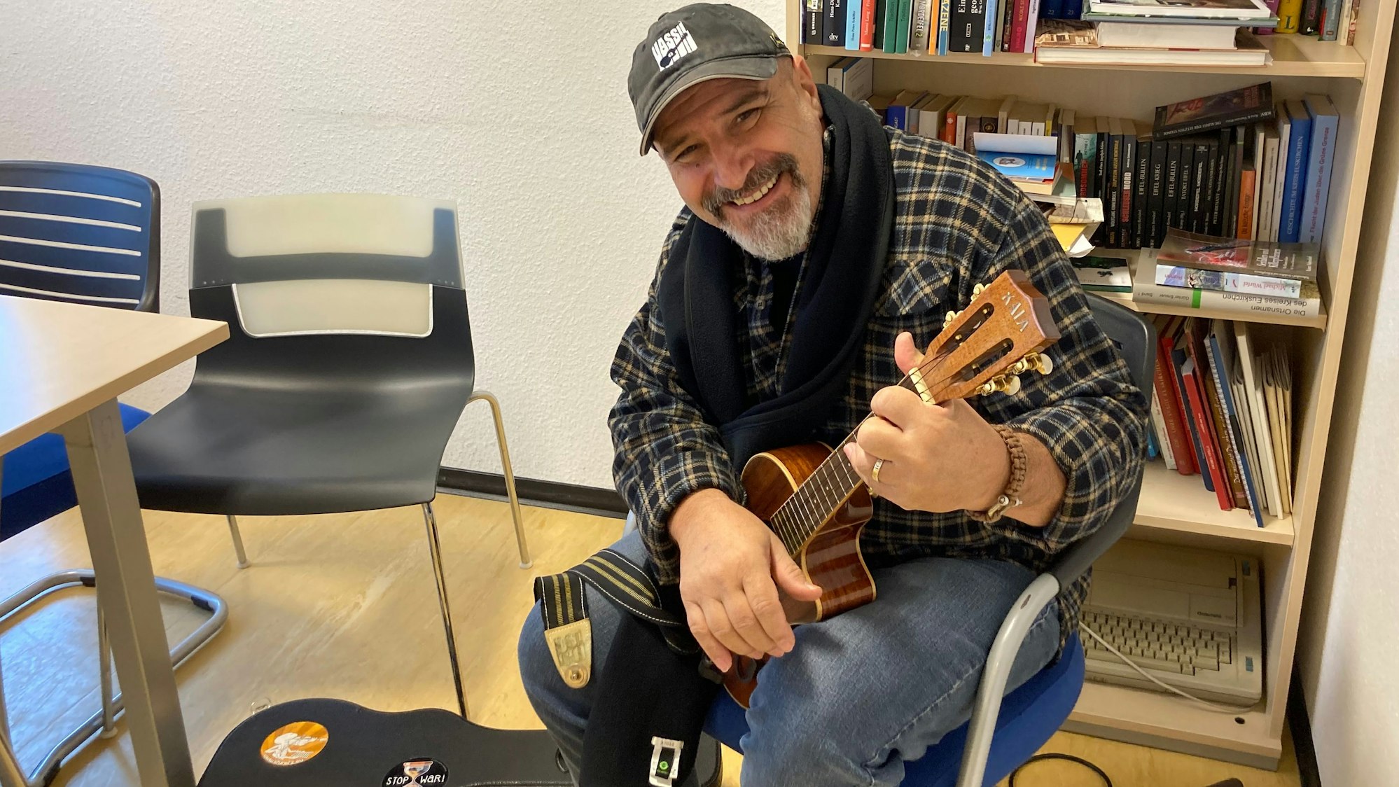 Der Musiker Vassil Svechtarov sitzt mit einem Saiteninstrument in den Händen vor einem Regal mit Büchern.
