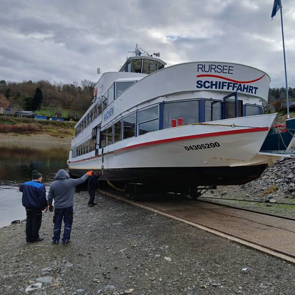 Die Mitarbeiter der Rurseeschifffahrt verfolgen, wie das weiße Schiff auf seinem Schlitten eine Rampe hinauf an Land gezogen wird.