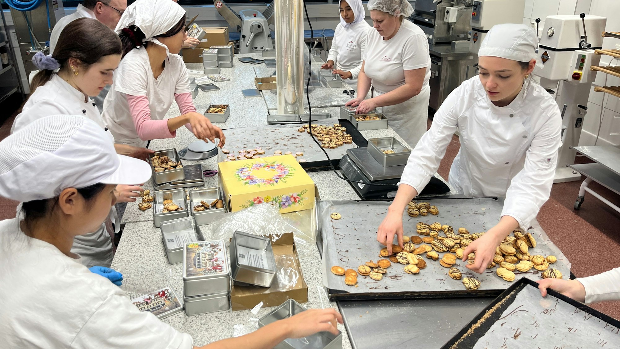 Junge Frauen in weißer Konditorenkleidung verpacken Plätzchen.