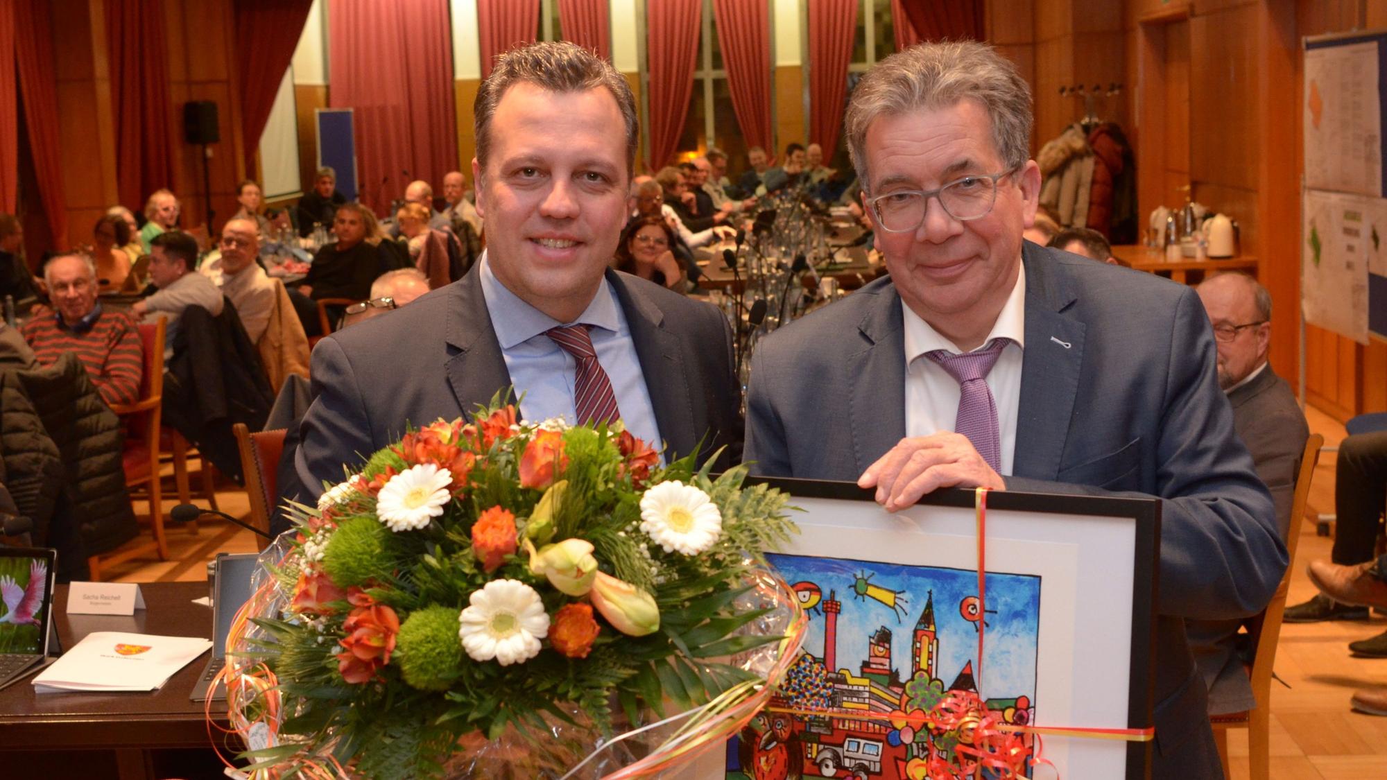Schmitz hält ein gemaltes Bild in der Hand, Reichelt einen Blumenstrauß.