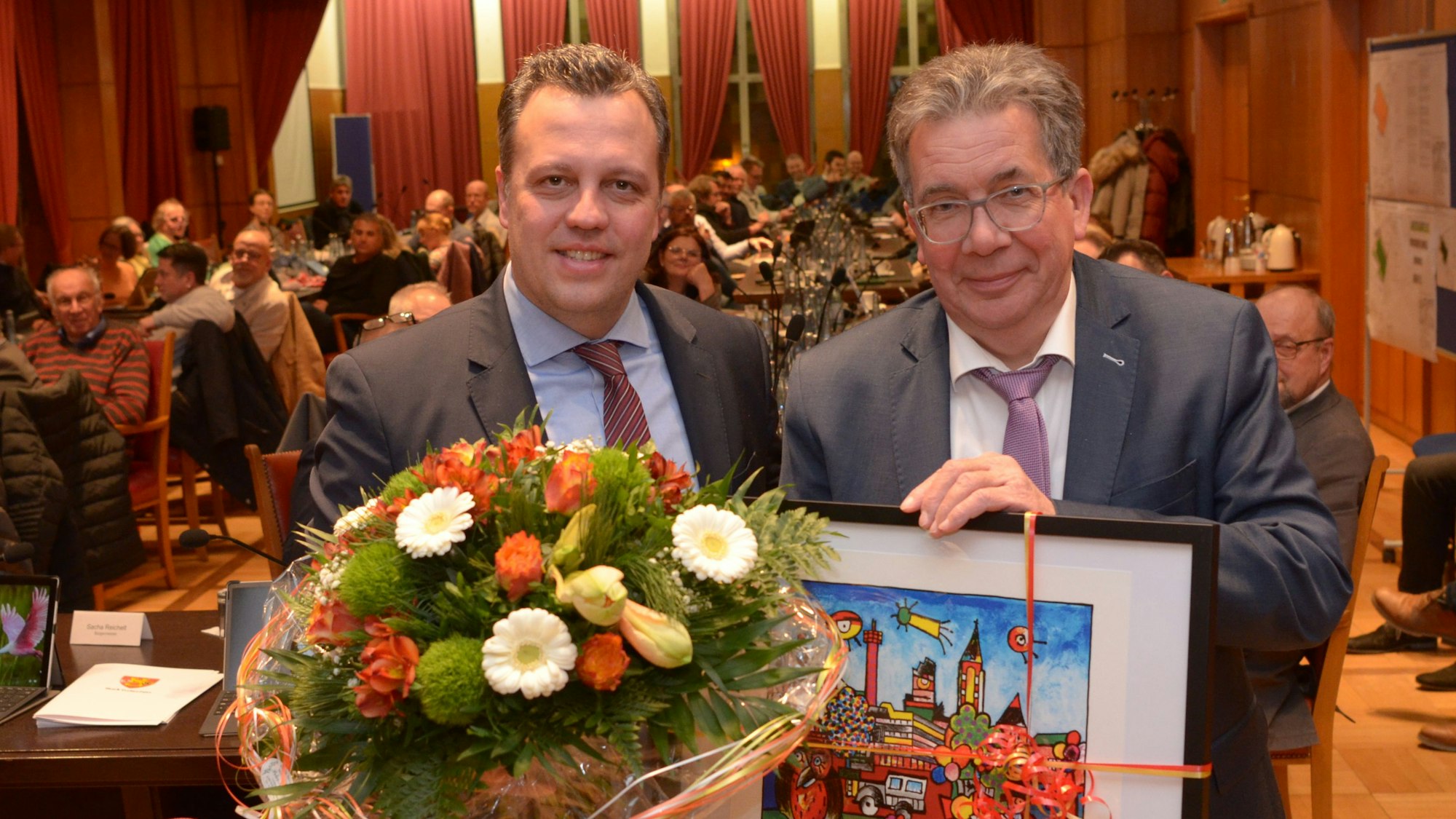 Schmitz hält ein gemaltes Bild in der Hand, Reichelt einen Blumenstrauß.
