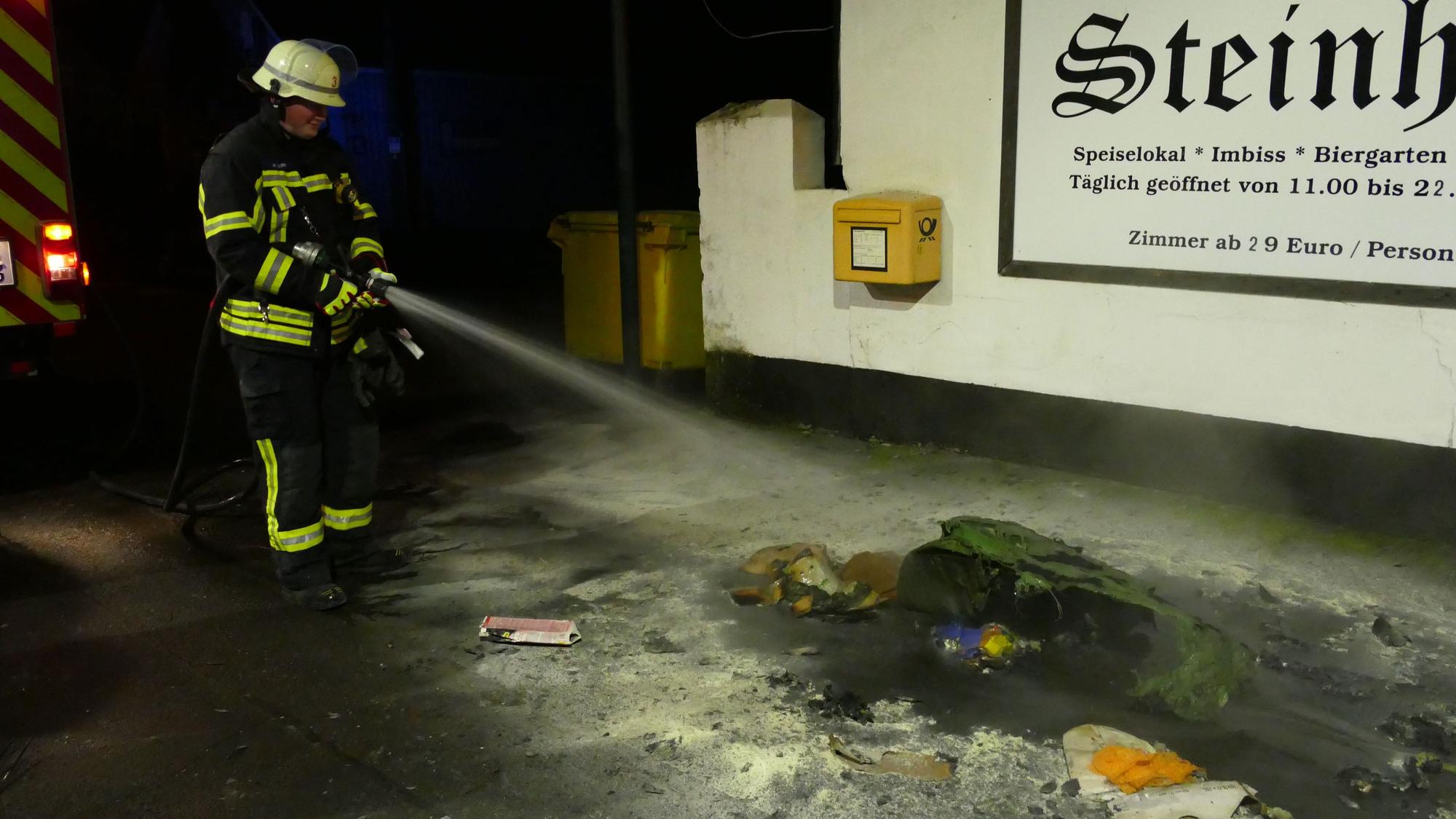 Ein Feuerwehrmann löscht eine brennende Papiertonne.