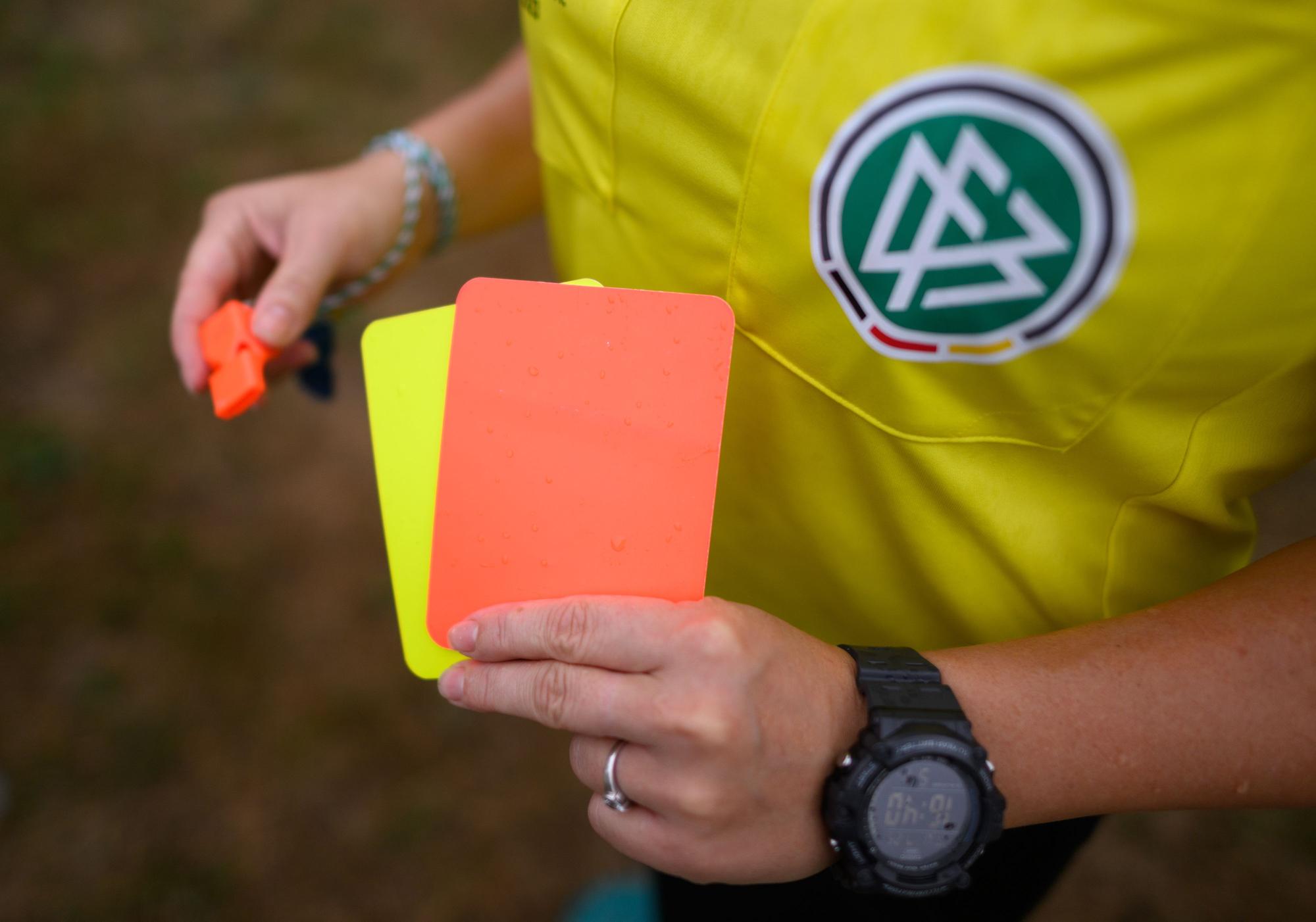 ARCHIV - 25.07.2023, Sachsen, Kamenz: Eine Schiedsrichterin, steht mit roter und gelber Karte auf einem Rasen und hält in der anderen Hand eine Trillerpfeife. 961 Mal kam es zu Spielabbrüchen im Amateurfußball. (zu dpa: «Referee verklagt DFB Schiri GmbH wegen Diskriminierung») Foto: Robert Michael/dpa +++ dpa-Bildfunk +++