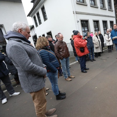 Mehrere Menschen auf einer Straße, am Rand liegen Messingsteine, die in die Straße eingesetzt werden sollen.