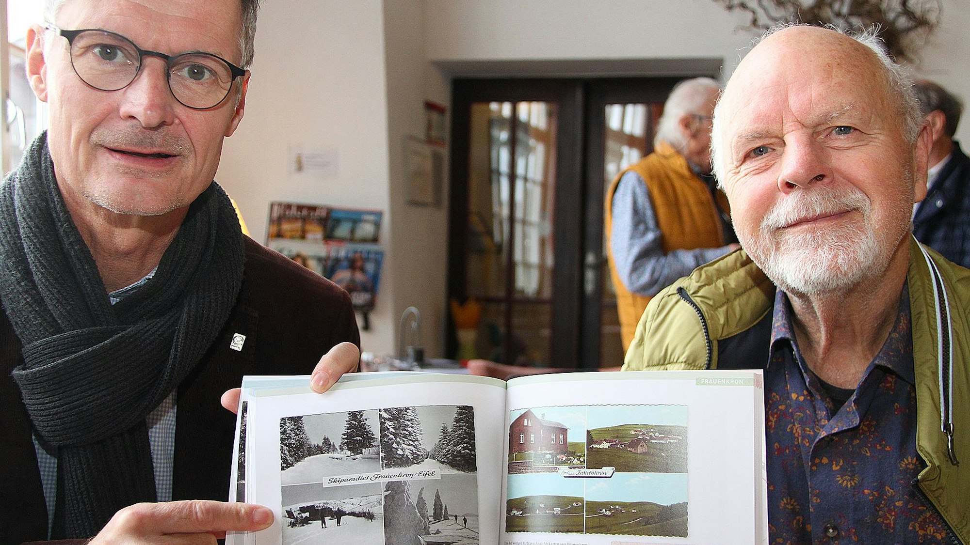 Zwei Männer halten ein Buch mit historischen Fotos in die Kamera.