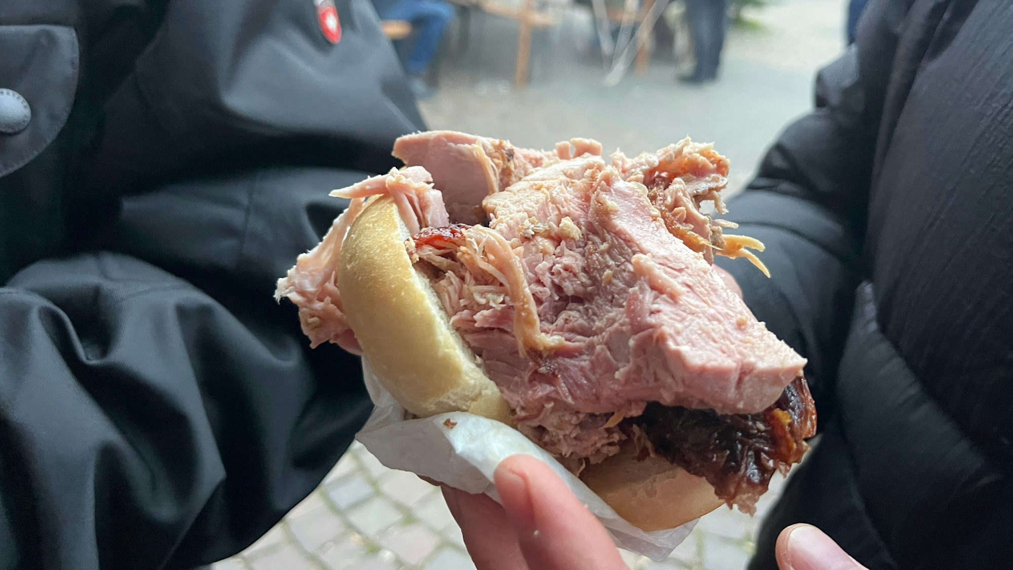 Ein Mann hält eine Portion Schweinefleisch im Brötchen in der Hand.