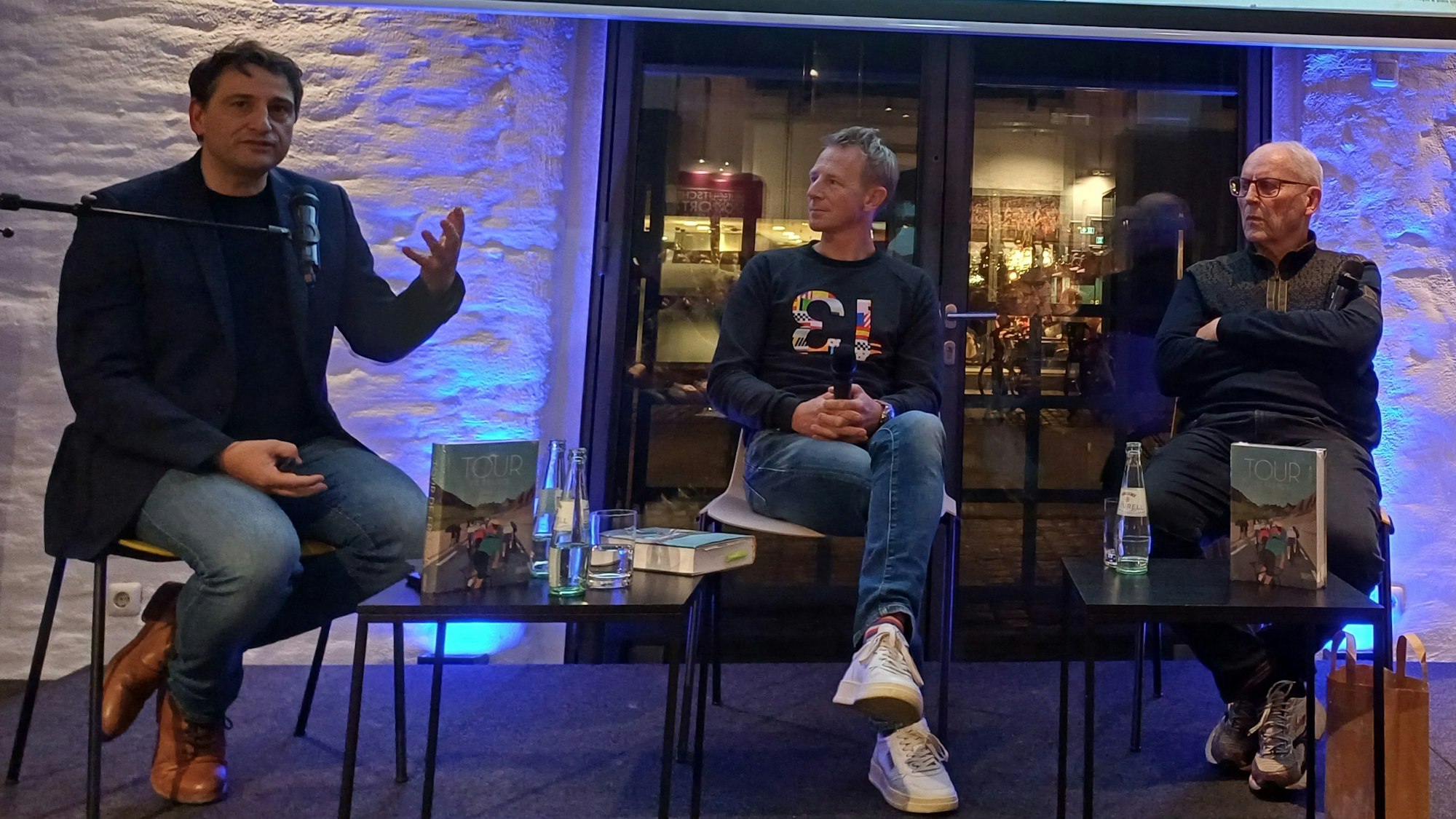 Drei Männer sitzen auf einer Bühne.