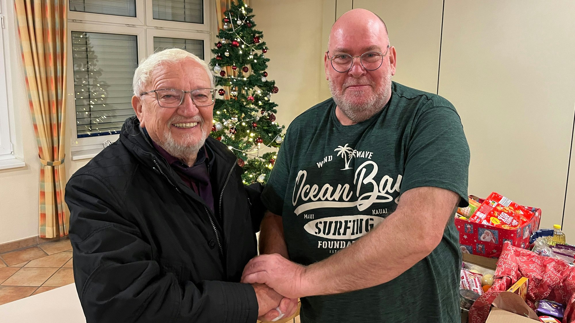 Zwei Männer reichen sich vor einem Weihnachtsbaum die Hände.