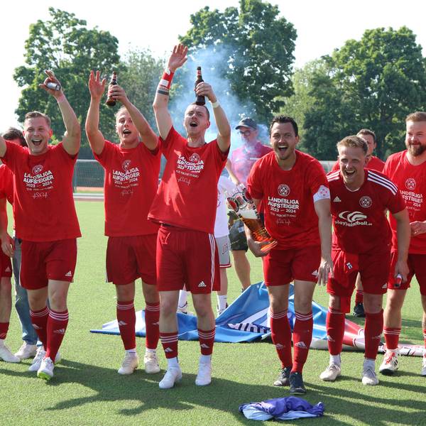 Die Spieler des TuS Zülpich freuen sich über ihren Aufstieg. Sie feiern, halten Bierflaschen und Arme in die Höhe und animieren die Fans.