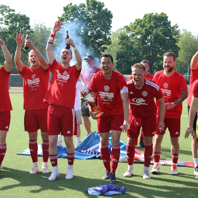 Die Spieler des TuS Zülpich freuen sich über ihren Aufstieg. Sie feiern, halten Bierflaschen und Arme in die Höhe und animieren die Fans.